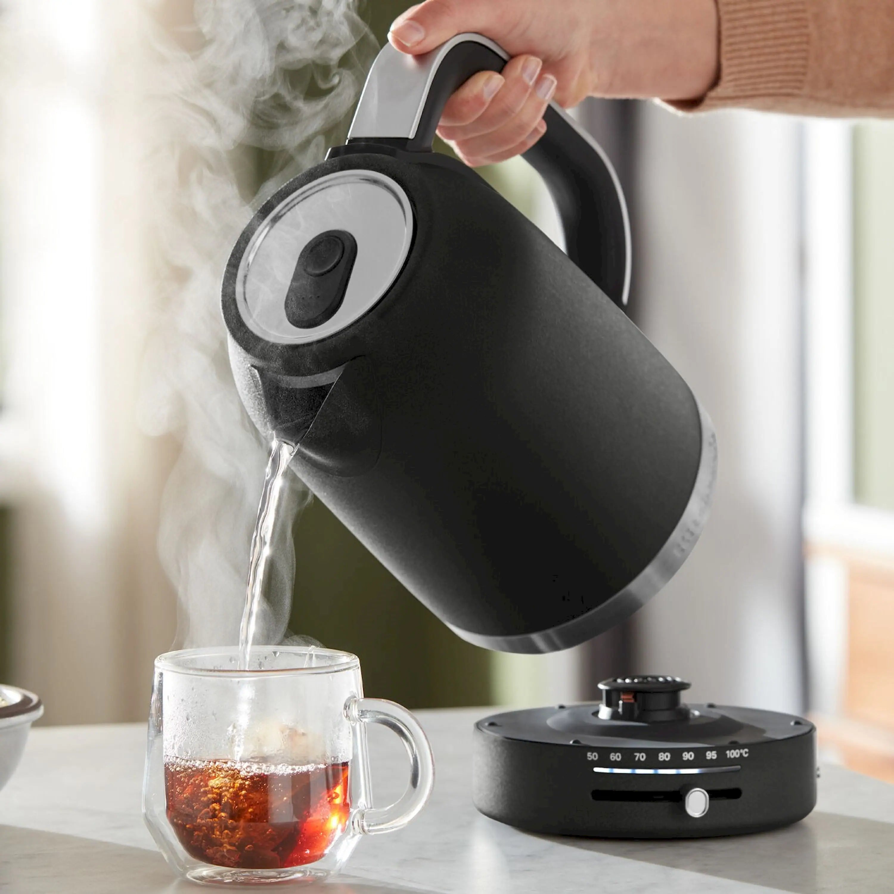 Black electric water kettle pouring hot water, with handle and lid on top.