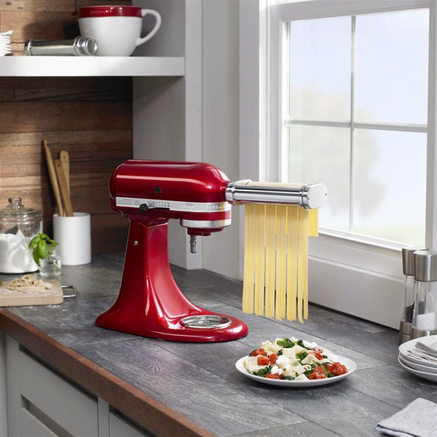Red stand mixer with stainless-steel pasta attachment and gold noodle strands