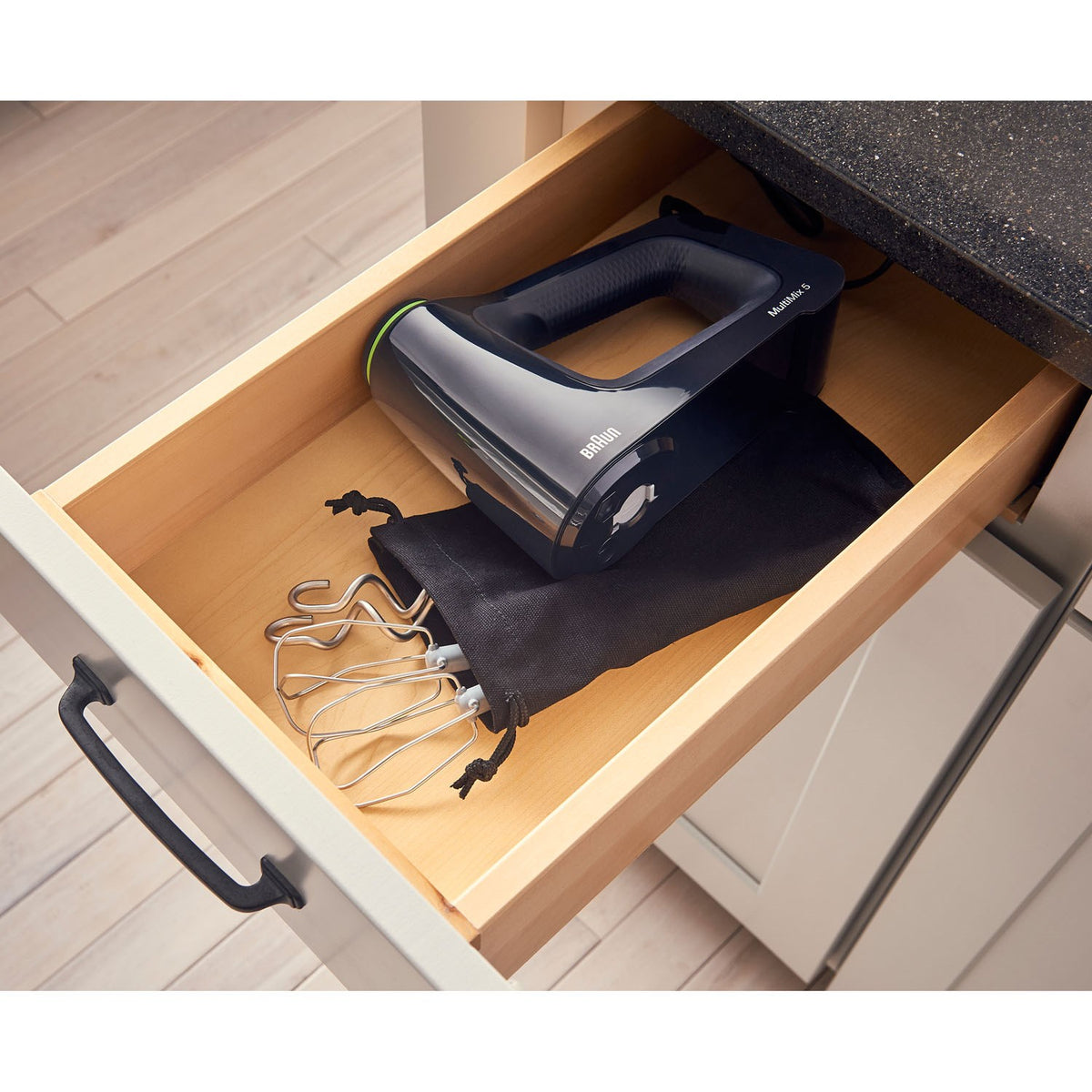 Black hand mixer with dough hooks and beaters placed in an open drawer compartment.