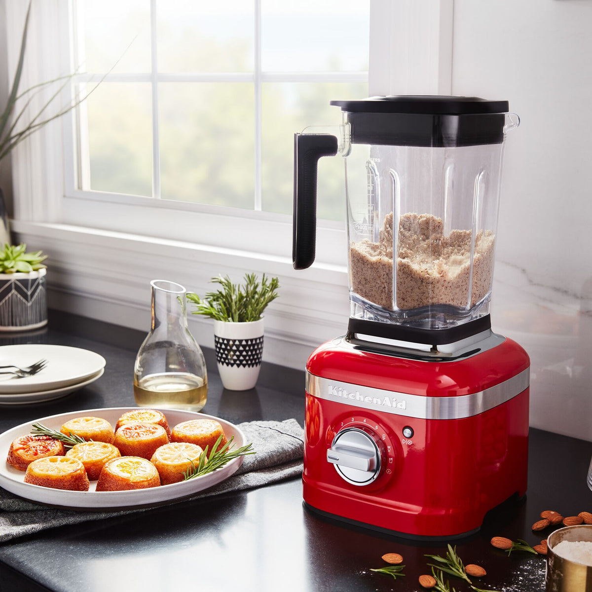 KitchenAid Passion Red blender on counter with grain-filled jar and pastries nearby
