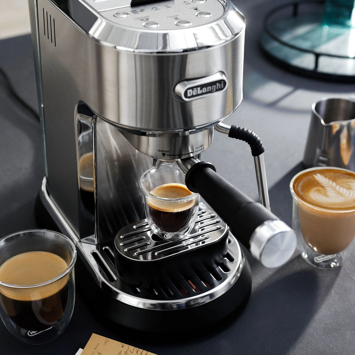Close-up stainless steel espresso machine with steam wand and frothing espresso in glasses