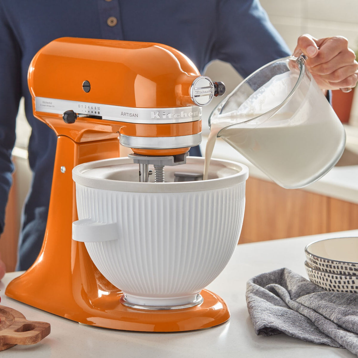 White ice cream maker attachment bowl on orange stand mixer with pour pitcher