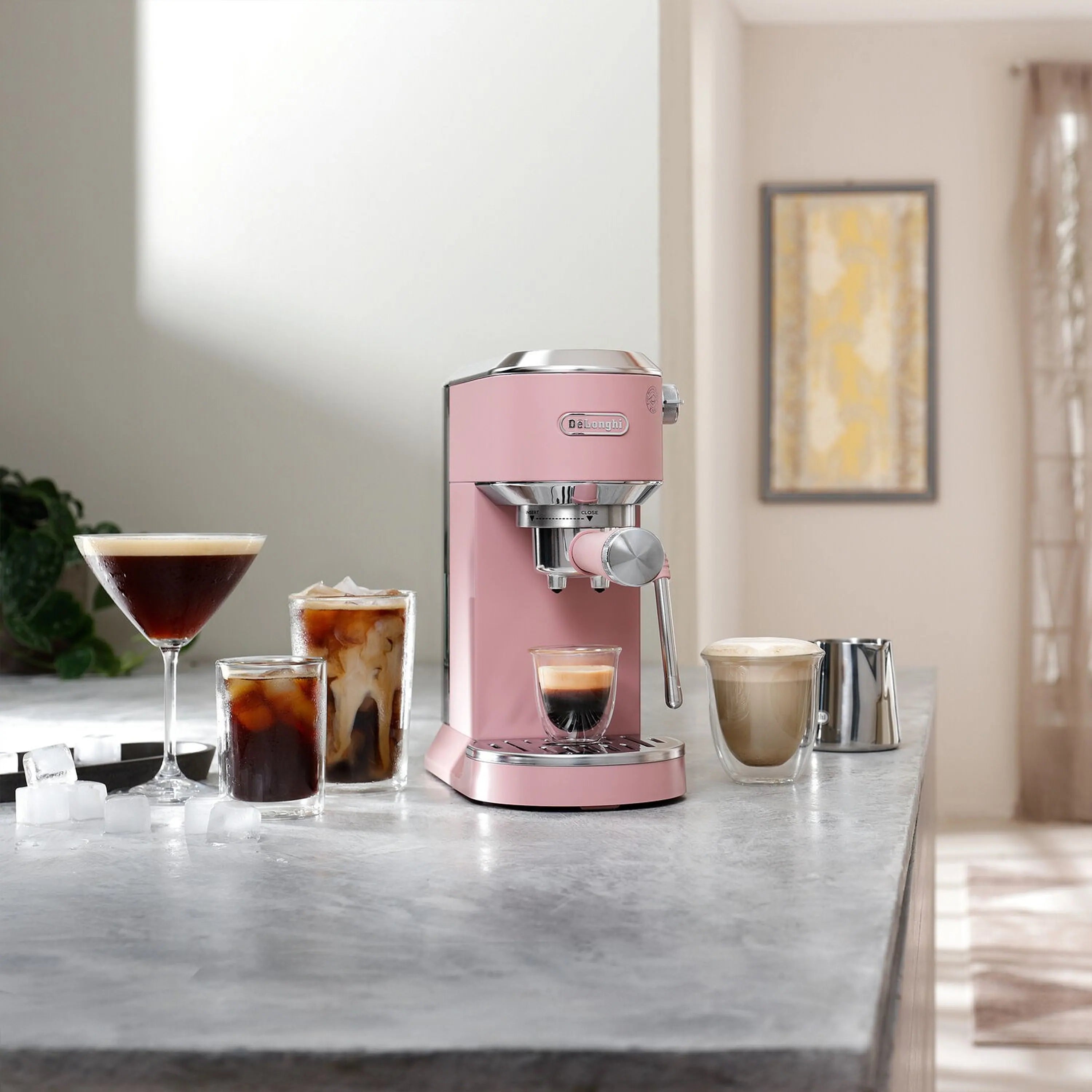 Pink De'Longhi espresso machine on countertop with three coffee cups and frothing wand