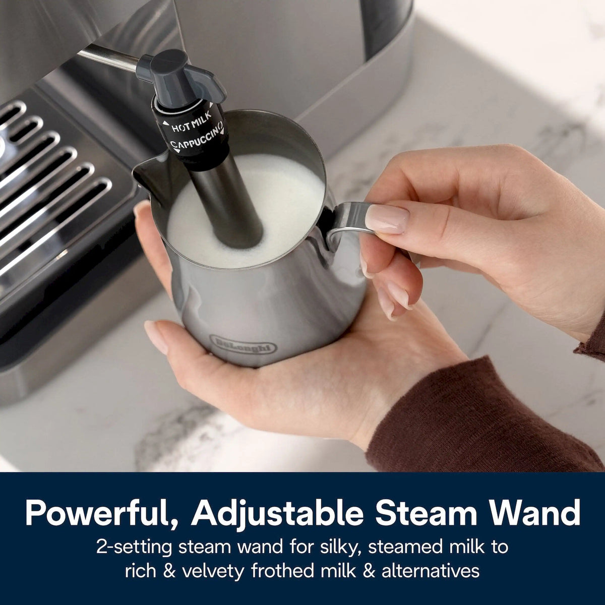Hands placing a stainless milk jug under the steam wand for frothing.