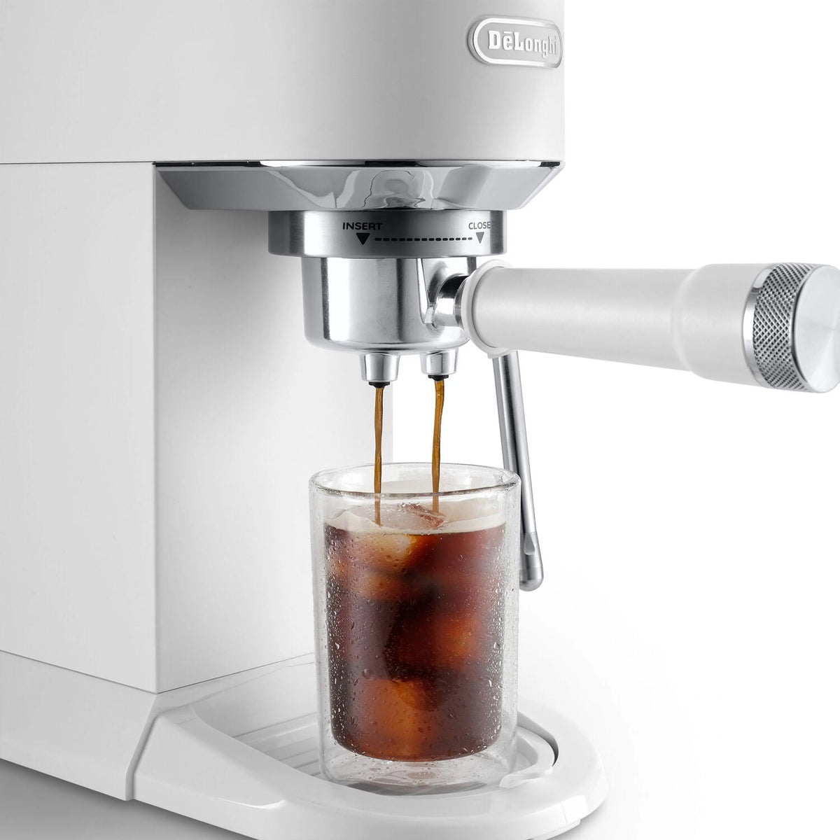 Espresso machine steam nozzles pouring into a tall glass of iced coffee