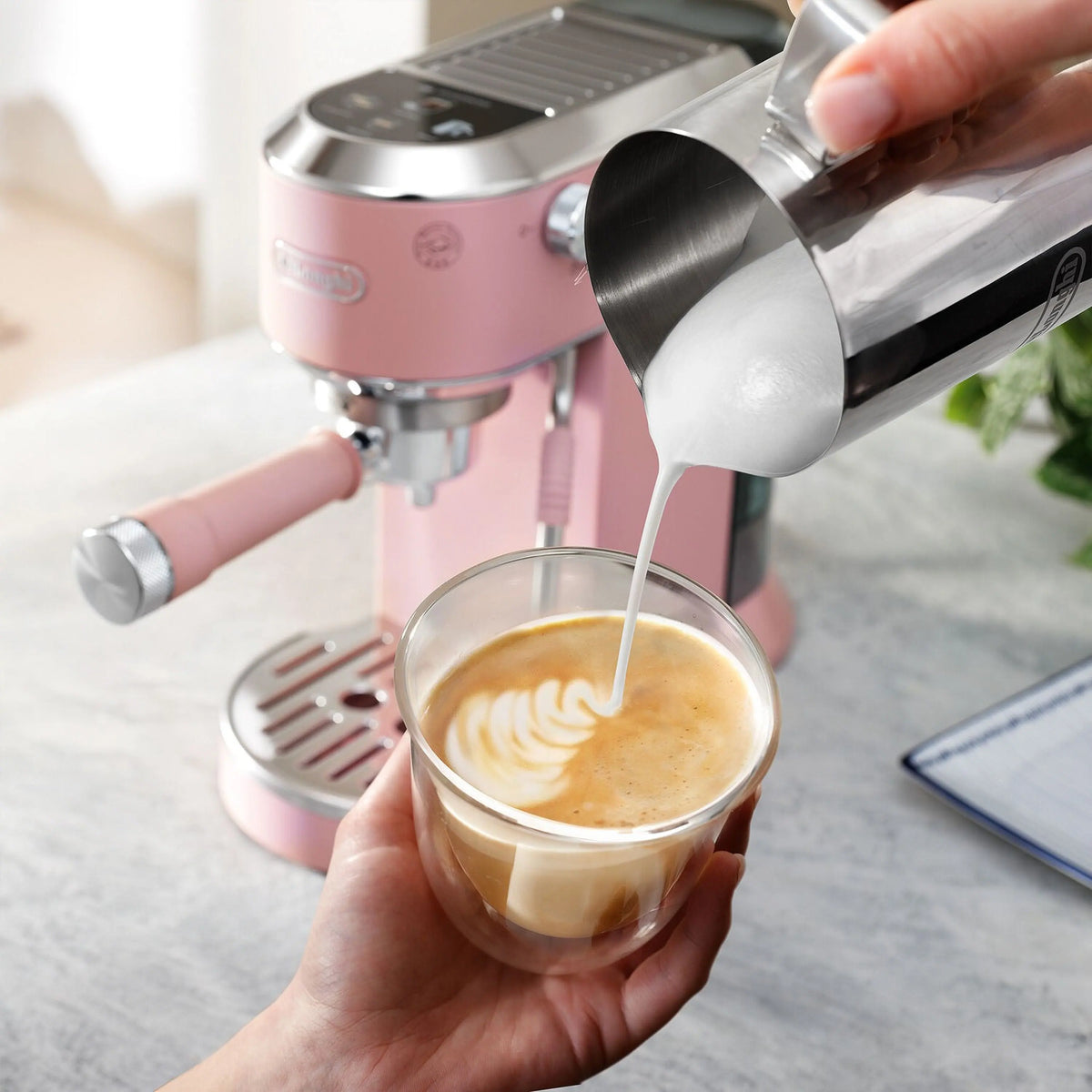 Pink De'Longhi espresso machine with frothing wand pouring into a milk-foam cup