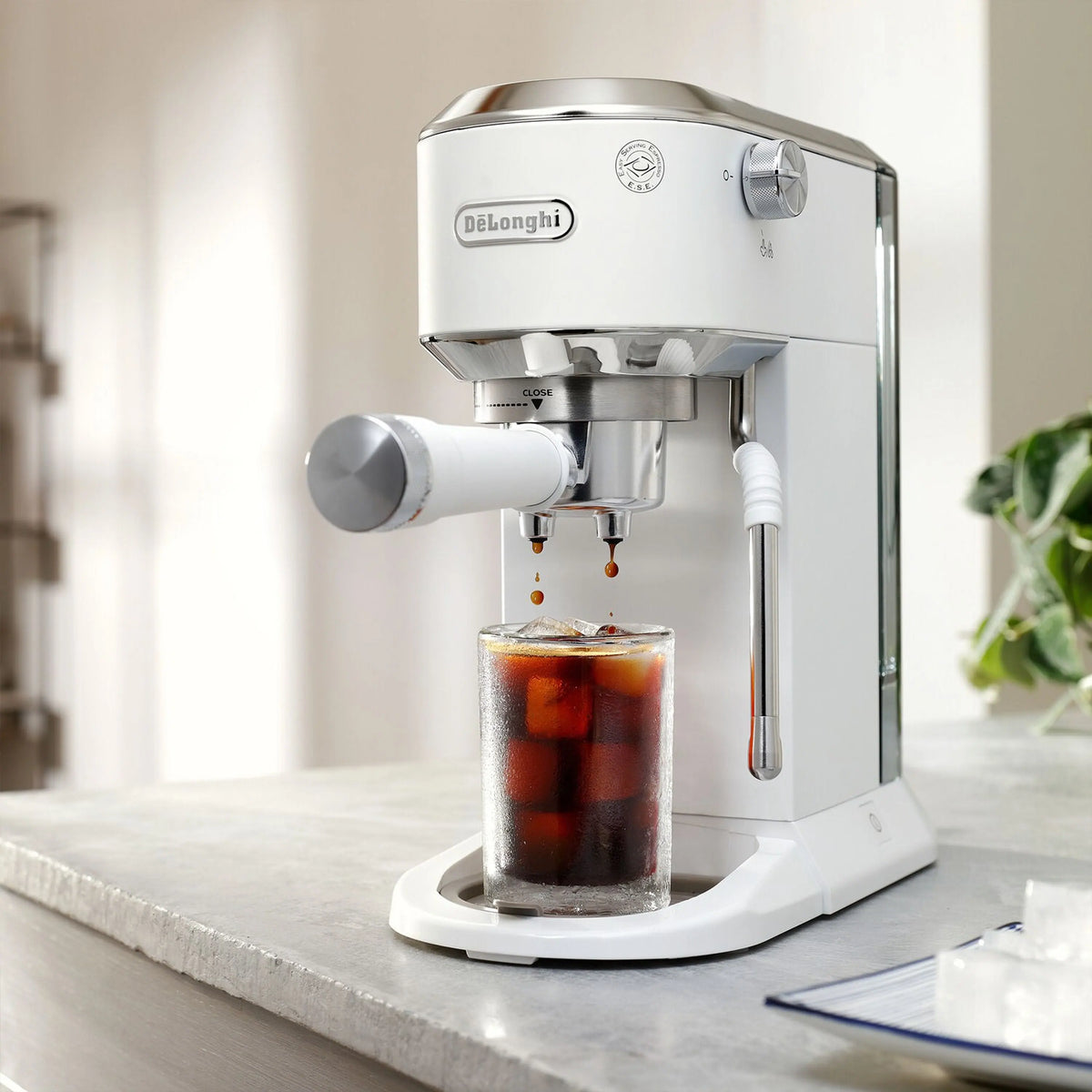 De'Longhi espresso machine dispensing iced coffee into a clear glass on a counter