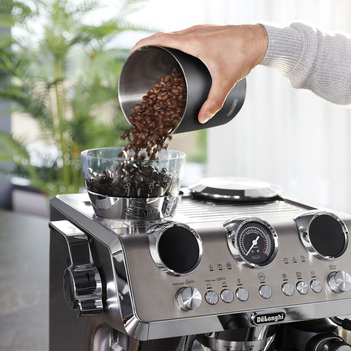 Stainless steel espresso machine hopper pouring coffee beans into grinding chamber