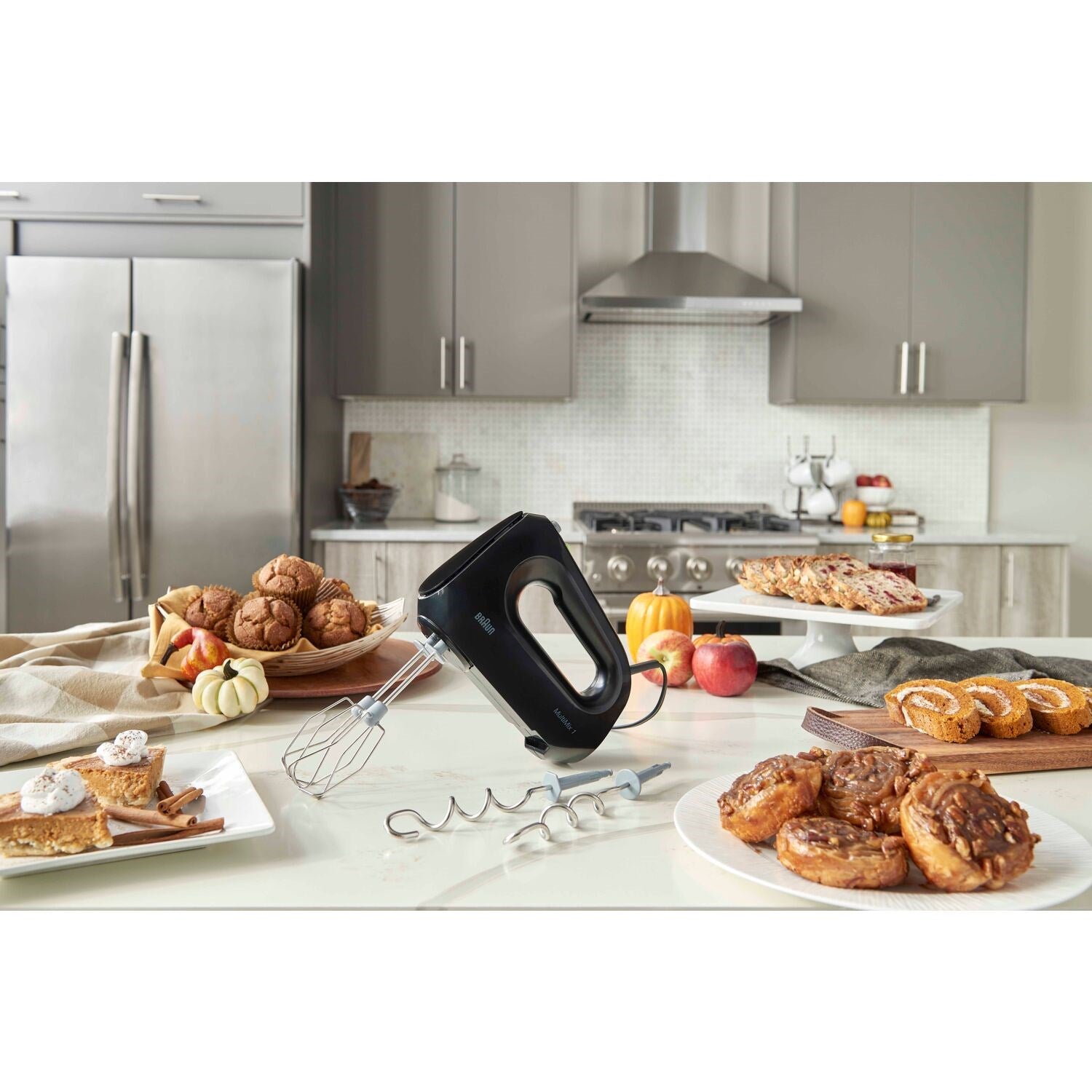 Black hand mixer with beaters and dough hooks on a countertop near mixing bowls