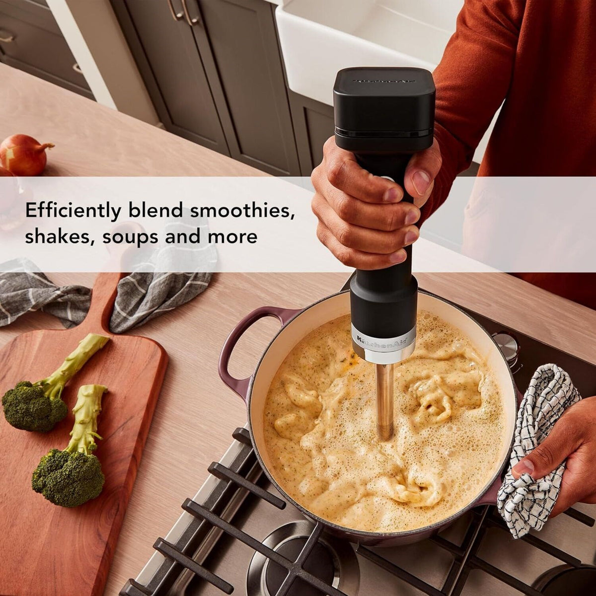 Cordless hand blender in black matte, blending into a pot of soup on a stove.