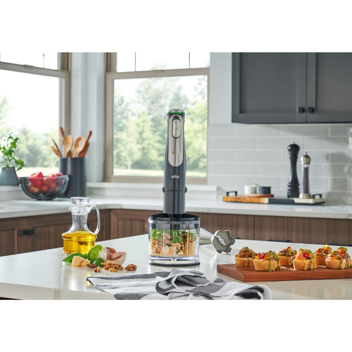 Braun hand blender standing on a countertop with a blending container and ingredients.