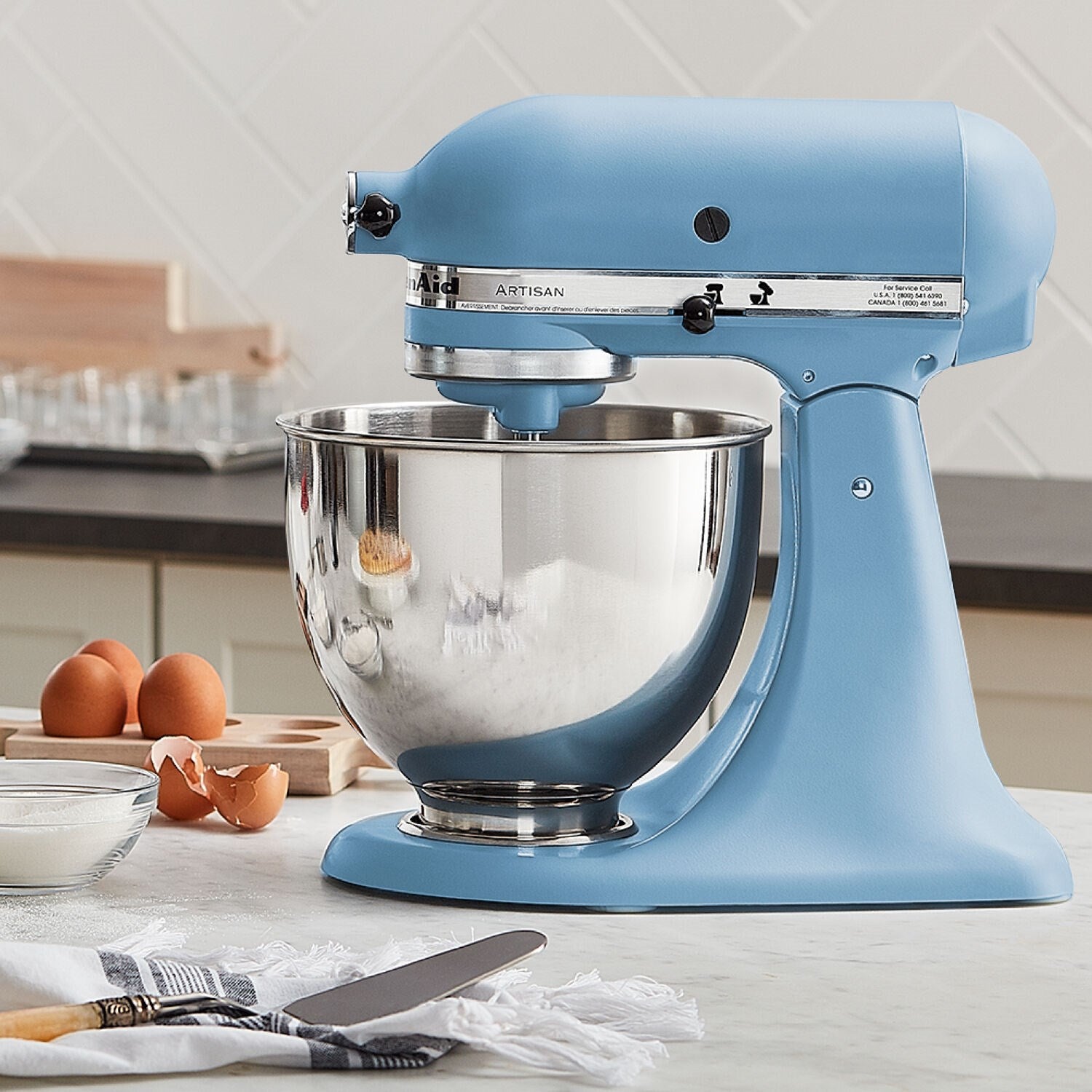 Blue tilt-head stand mixer with stainless bowl and eggs nearby on the counter