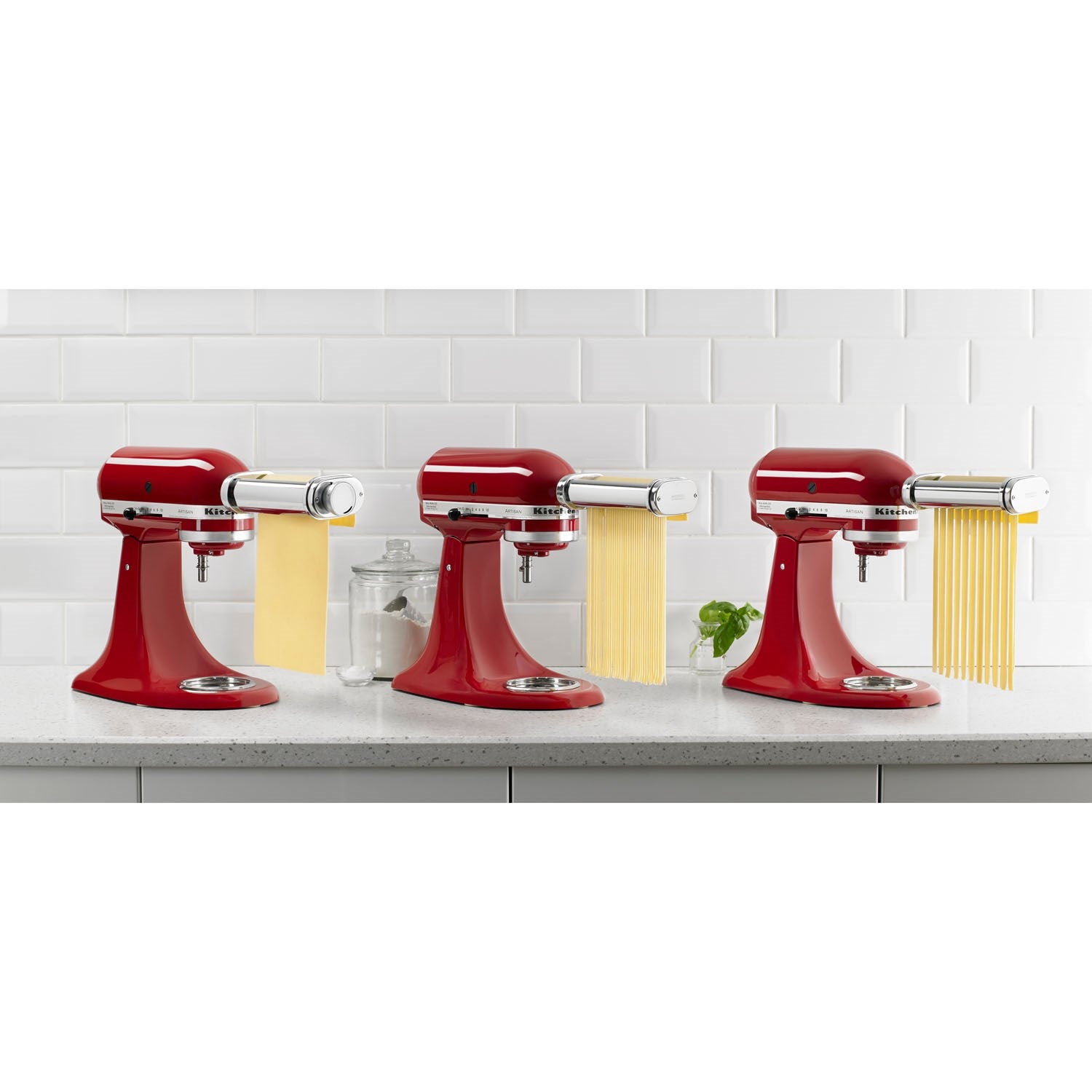 Three red stand mixers with pasta roller attachments producing yellow noodles
