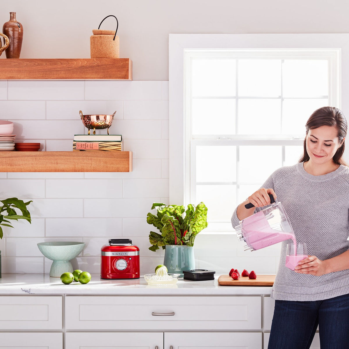 Woman pouring pink smoothie from blender pitcher into a glass in a bright kitchen
