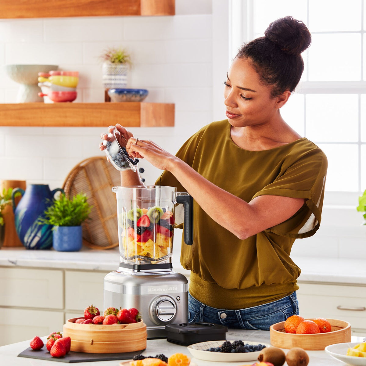 KitchenAid blender on countertop with purple smoothie and woman pouring into glass