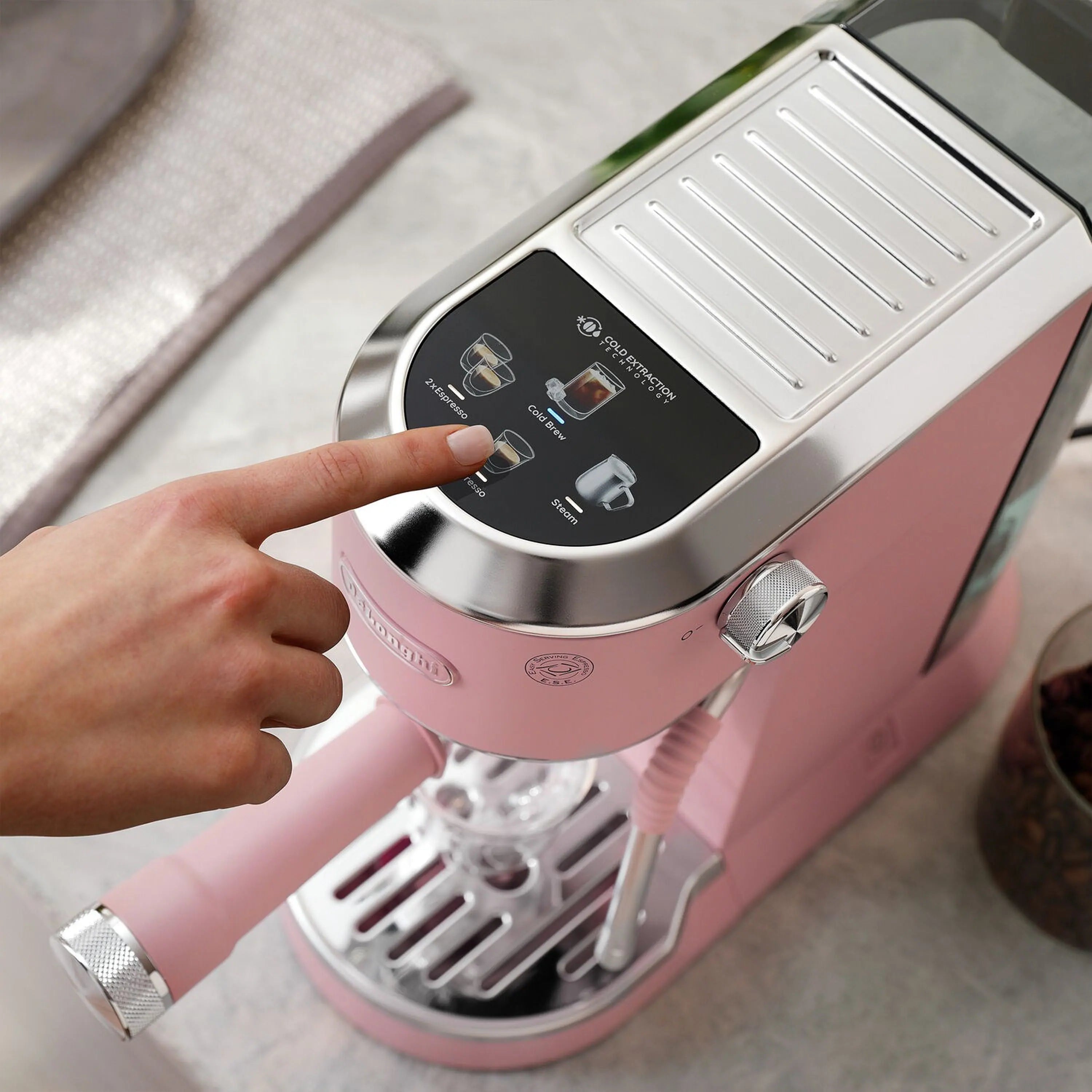 Pink espresso machine showing top control panel with user hand adjusting settings