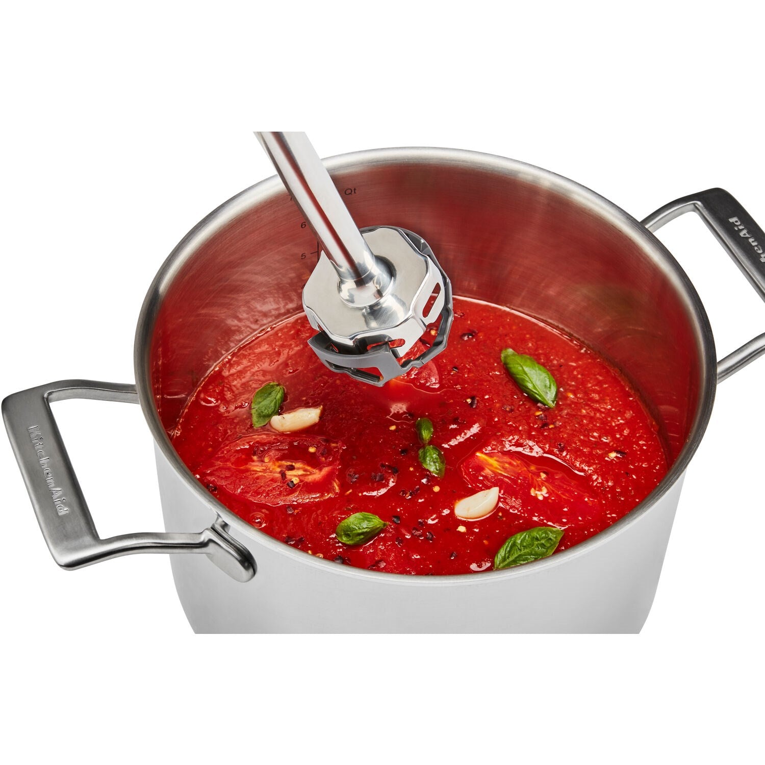 Immersion blender blending red sauce in a pot with scattered herbs