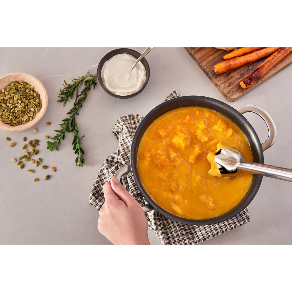 Hand blender stirring thick orange soup in a pot with immersion shaft