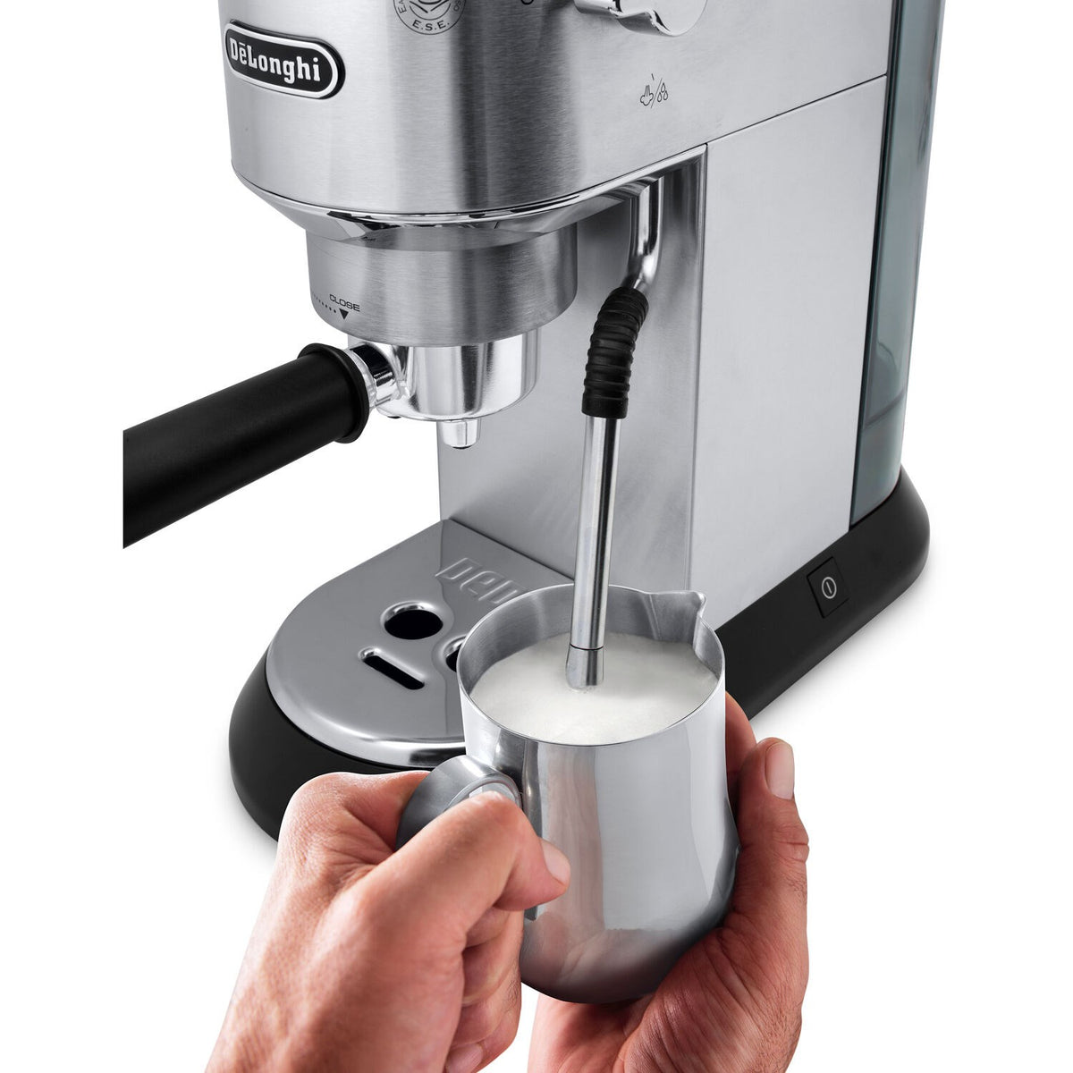 Hands holding a cup while the espresso machine steam wand froths milk