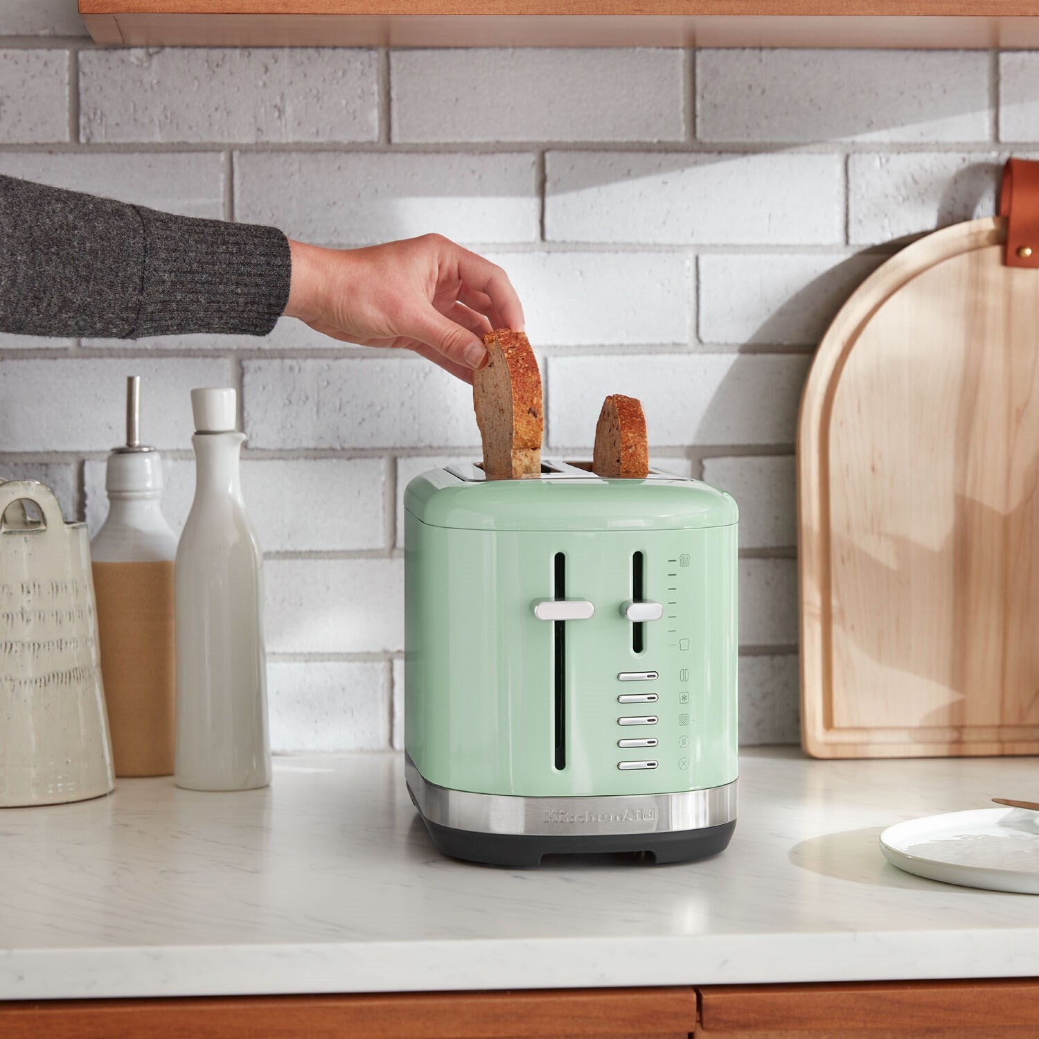 KitchenAid 2-slice toaster in pistachchio green on countertop with bread being inserted