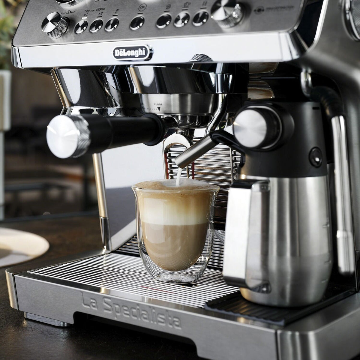 Stainless steel espresso machine steaming milk into a clear cup on drip tray