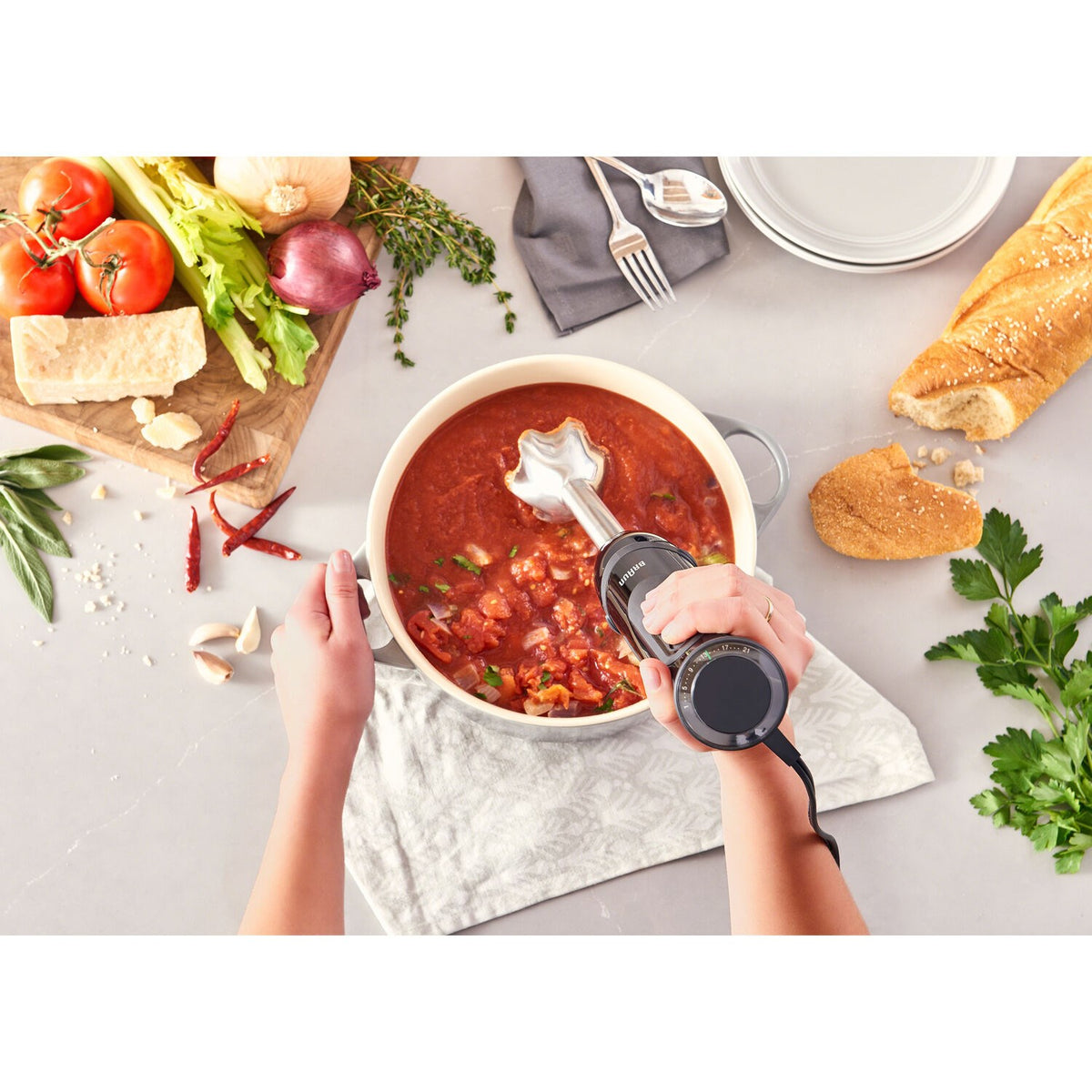 Hand blender blending red sauce in a bowl with immersion attachment