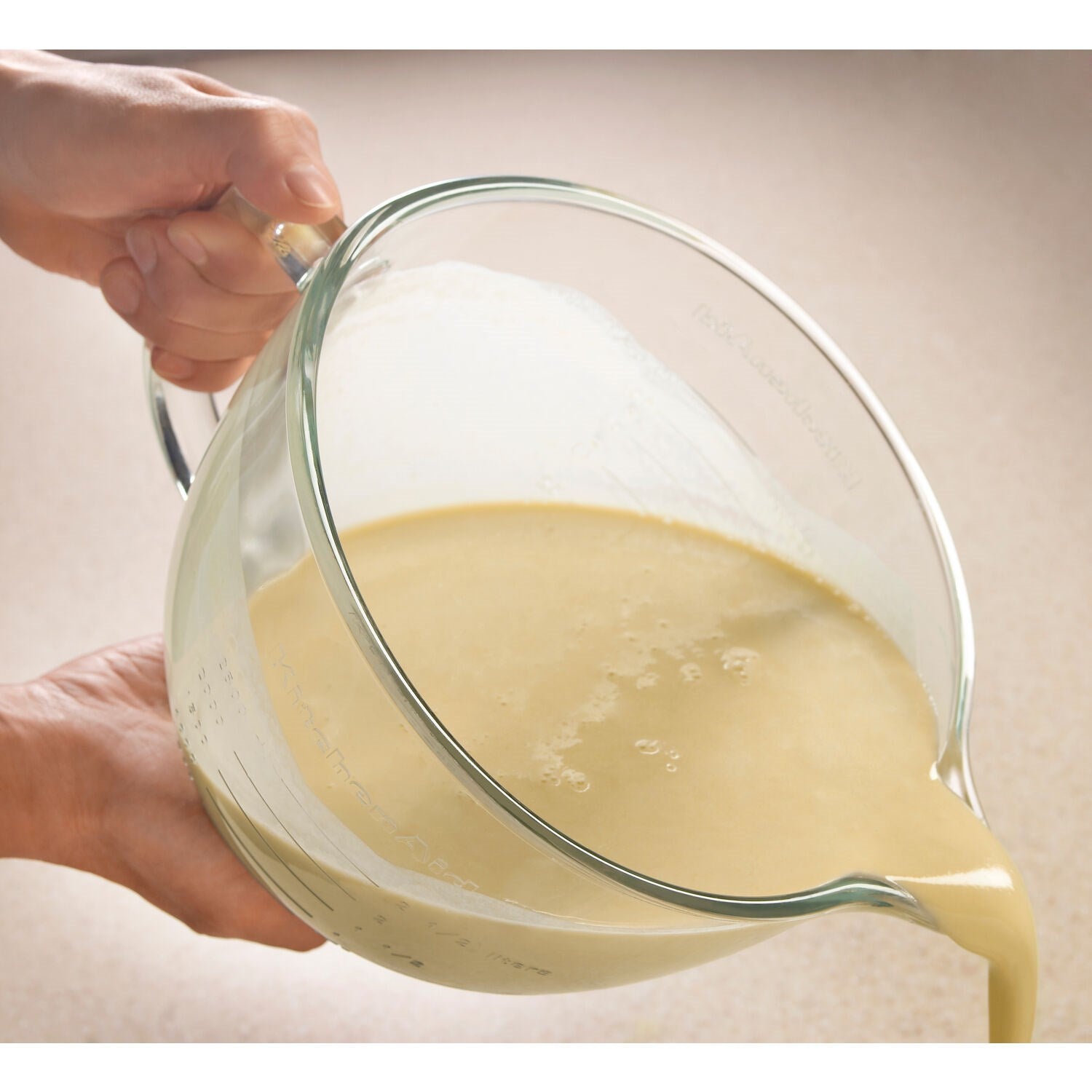 Clear glass mixing bowl with handle while pouring batter from a pitcher