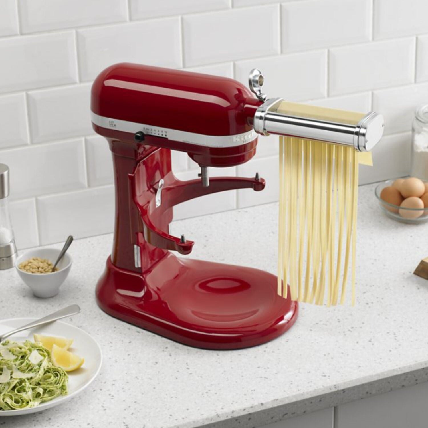 Pasta roller attachment on red stand mixer making long yellow spaghetti-style noodles