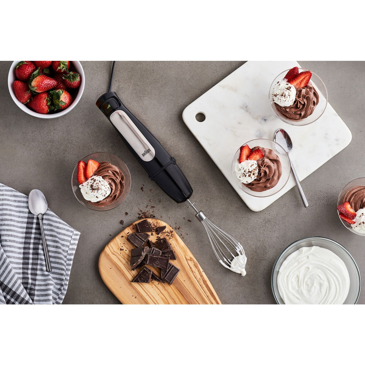 Braun hand blender with black motor base beside bowls of desserts and cream