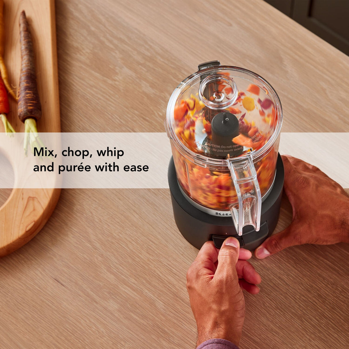 Hands turning a black cordless chopper with a clear cup filled with chopped food