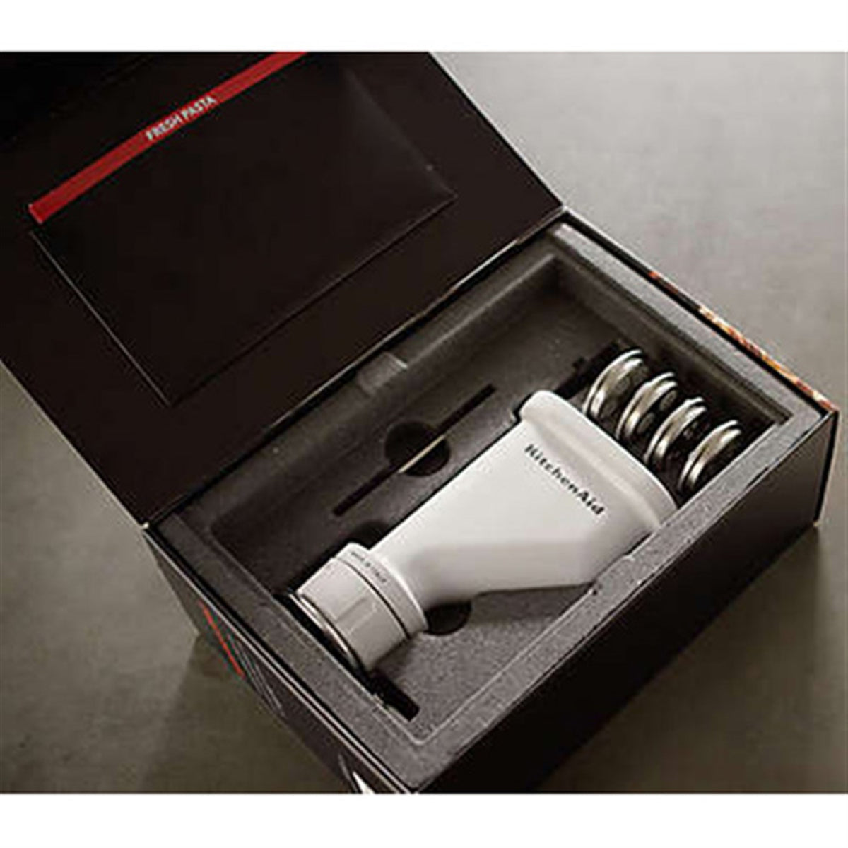 White KitchenAid pasta press attachment inside its open retail box with accessories.