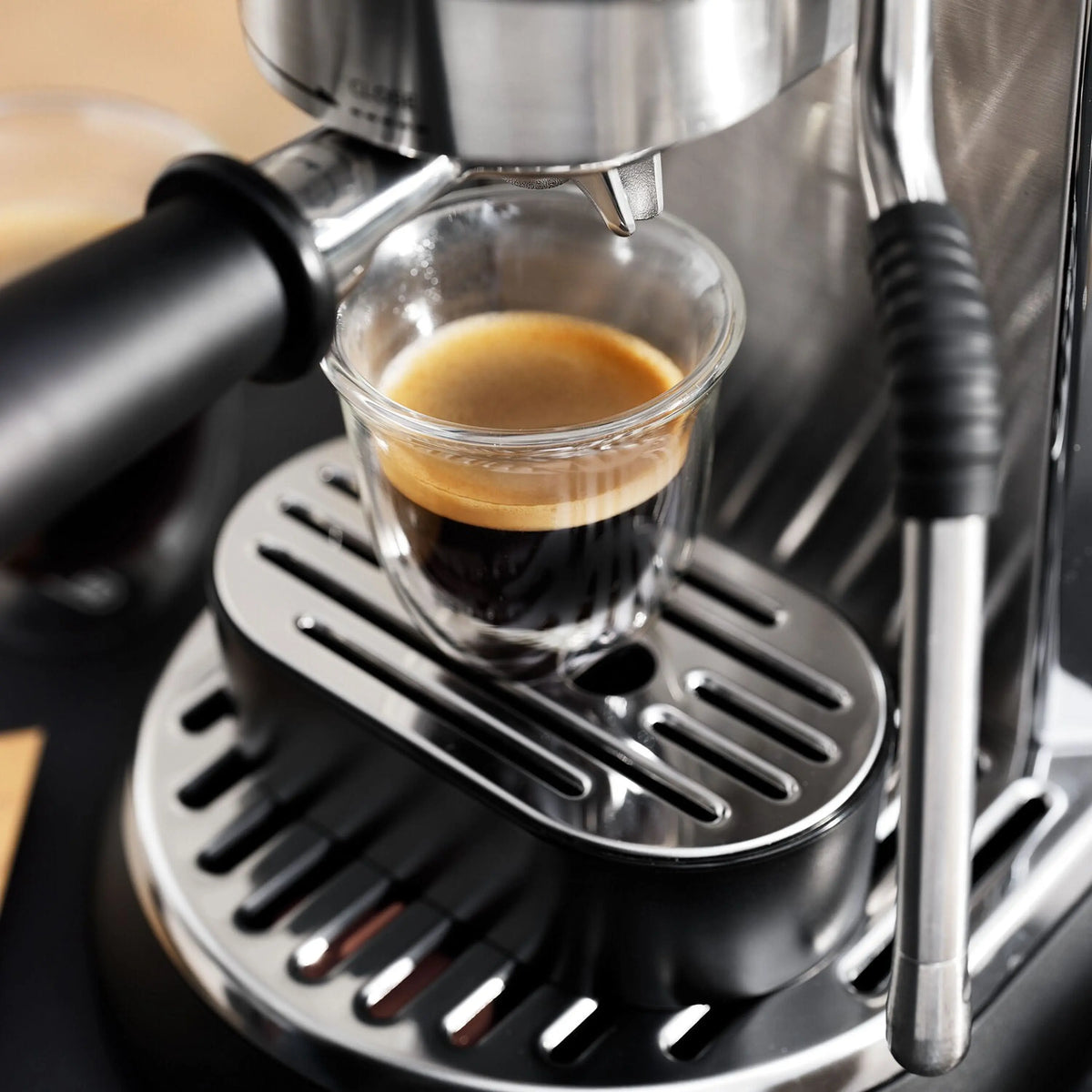 Glass cup of espresso beneath the machine spout on the drip tray