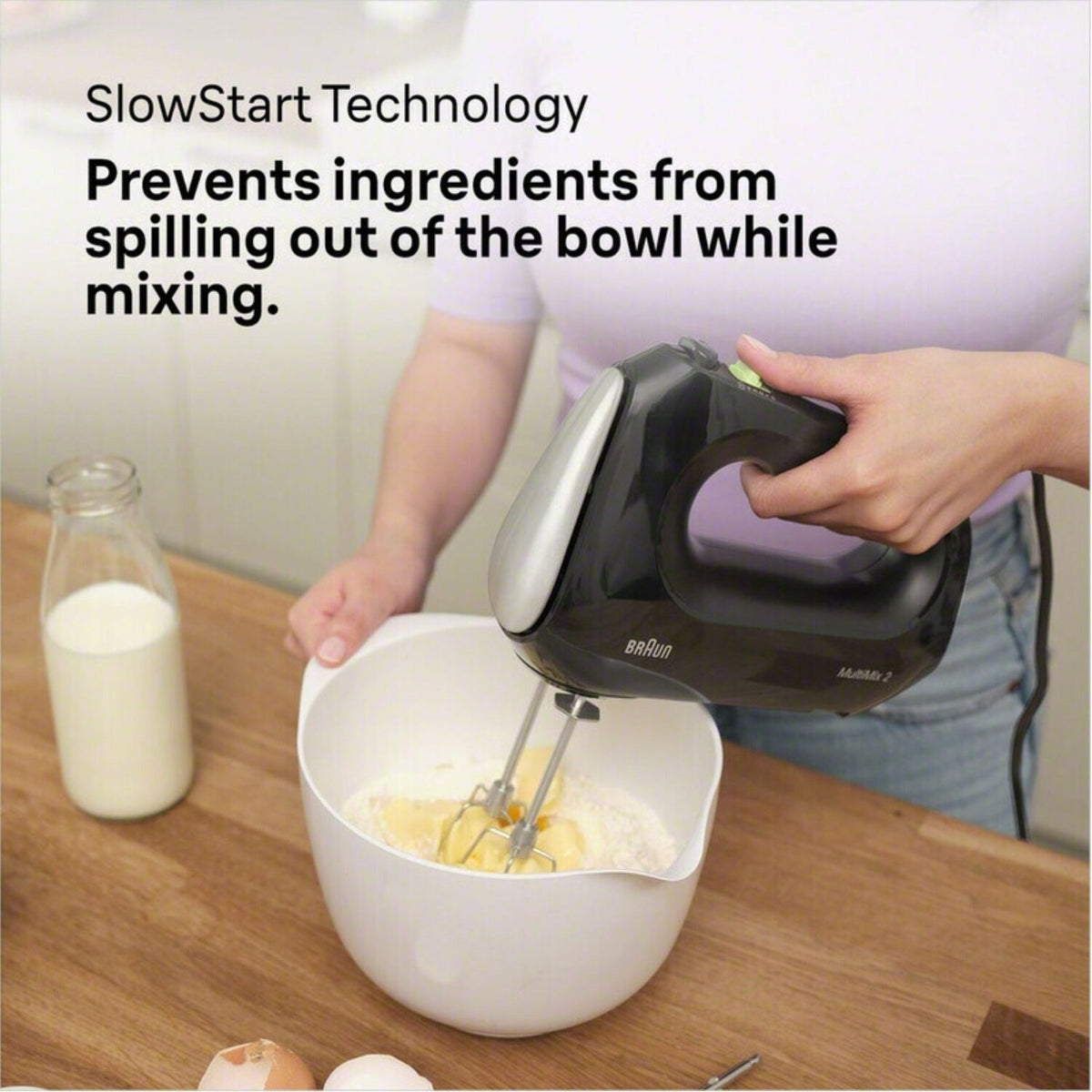 Black hand mixer blending batter with beaters over a white mixing bowl