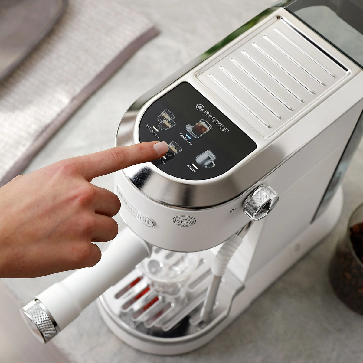 Hand turning a knob on stainless espresso machine control panel near the steam wand