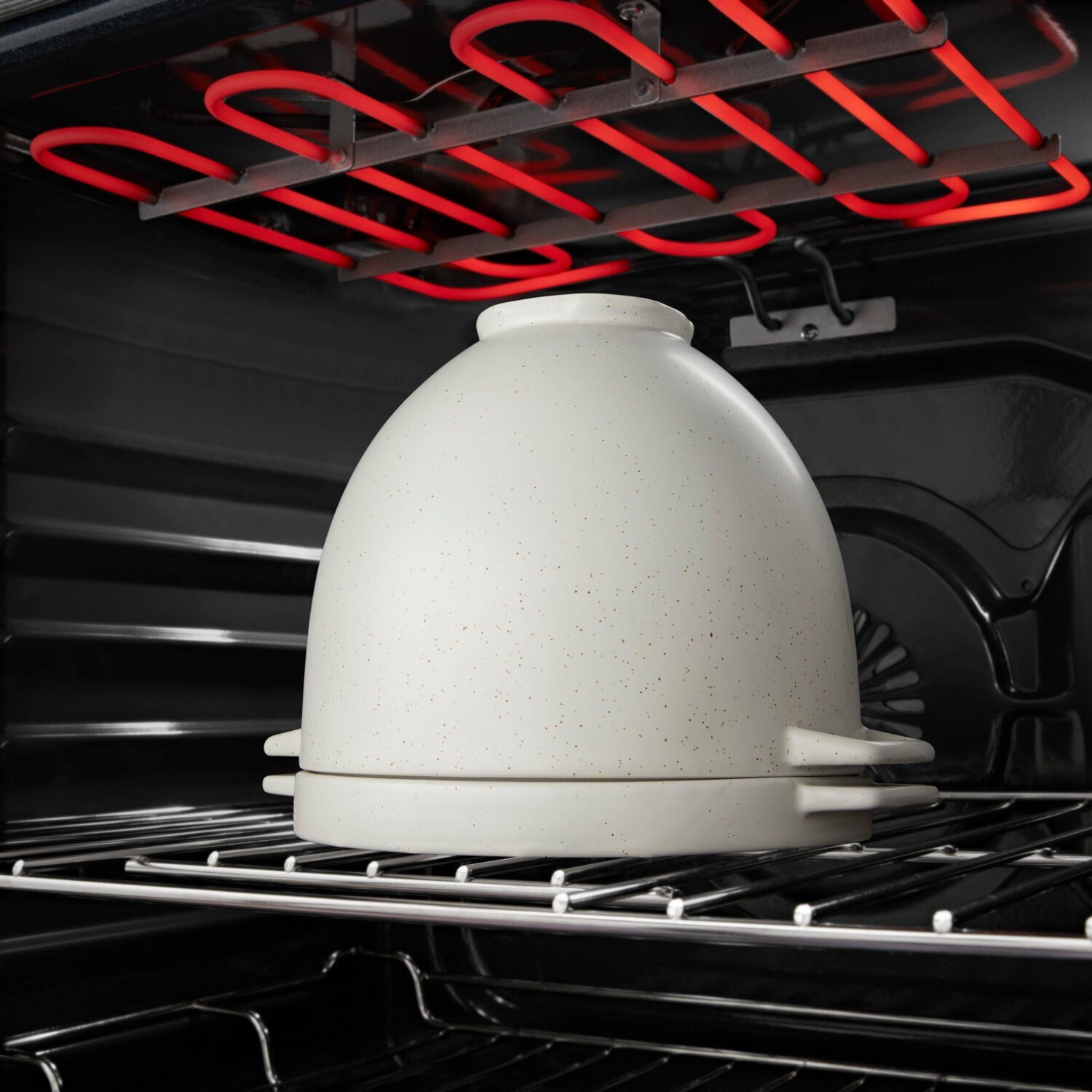 Bread baking bowl with lid, light speckled ceramic, on an oven rack