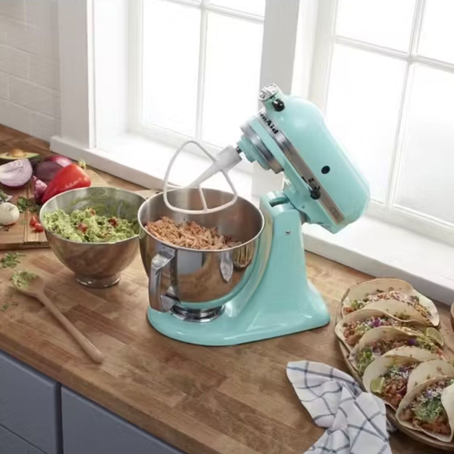 Aqua tilt-head stand mixer on countertop with mixing bowls and paddle attachment