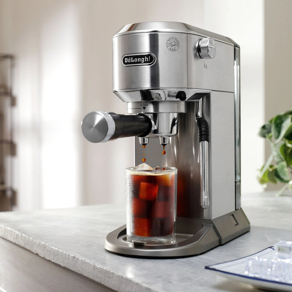 Stainless espresso machine dispensing dark coffee into a clear cold cup