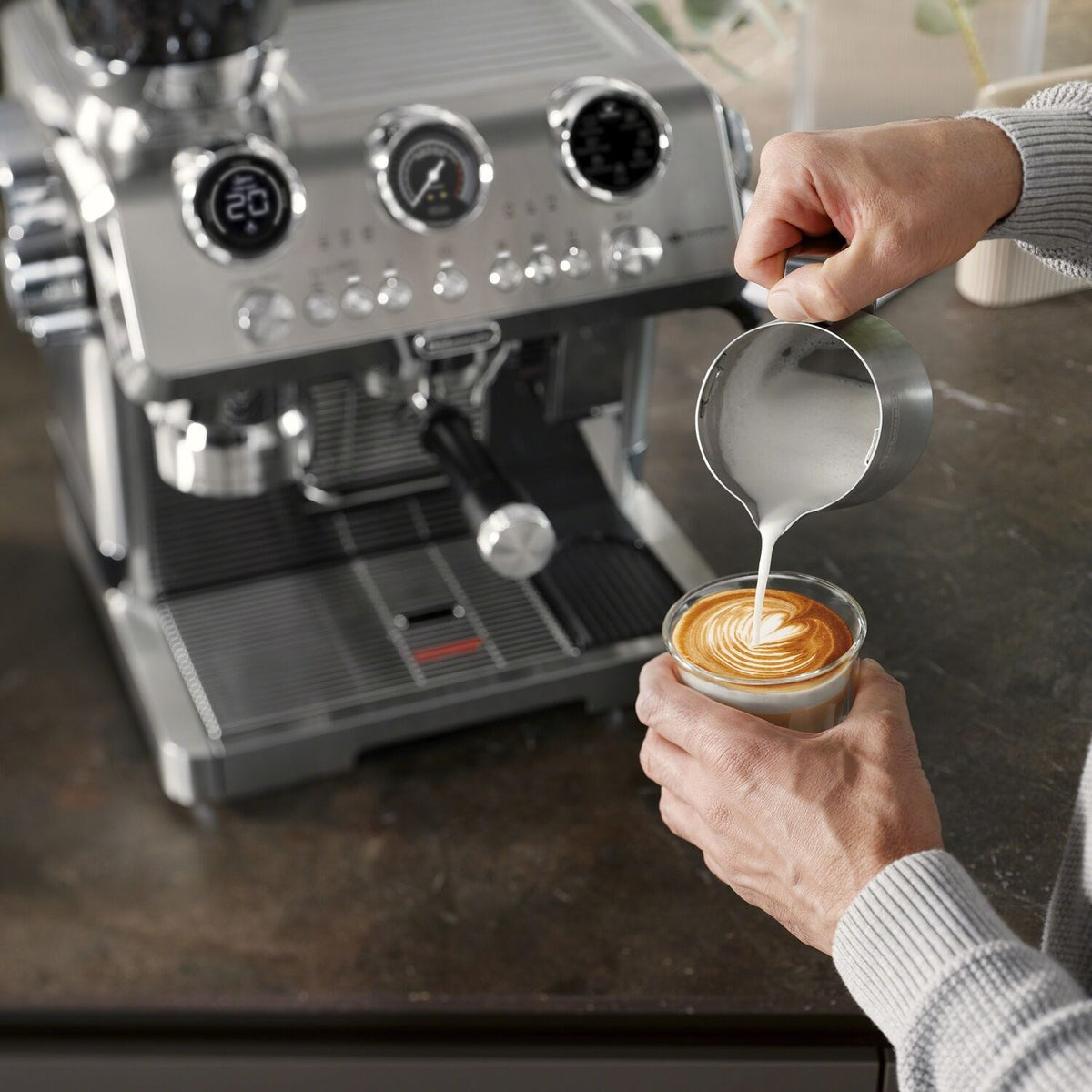 Stainless steel espresso machine with frothing pitcher pouring into a small cup