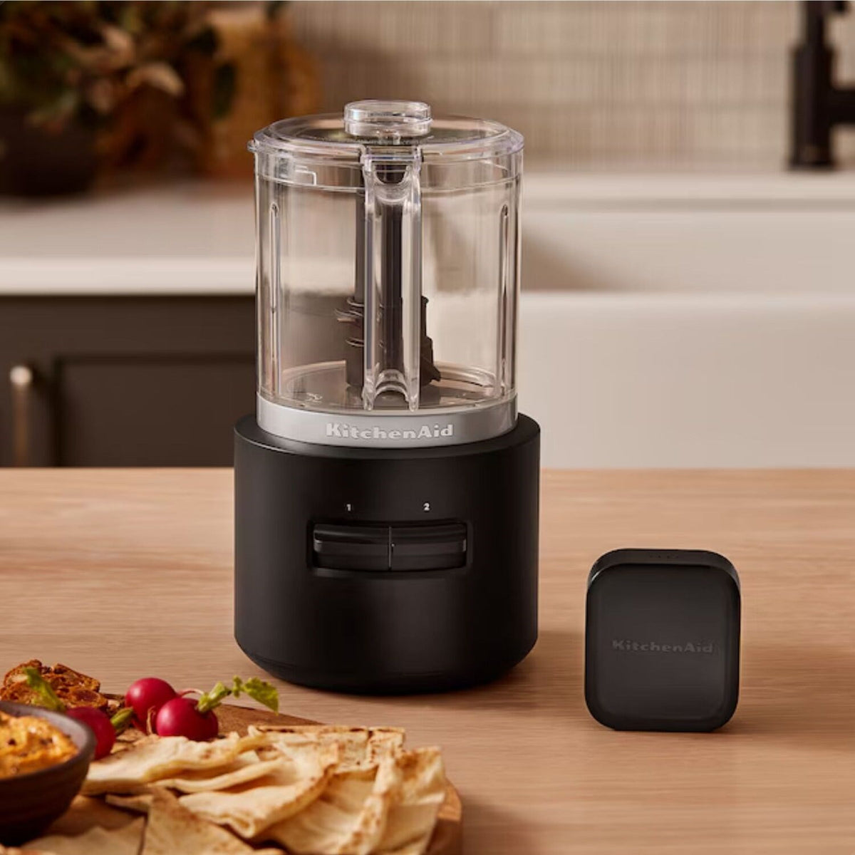 Black matte cordless chopper with clear bowl and separate battery pack on counter