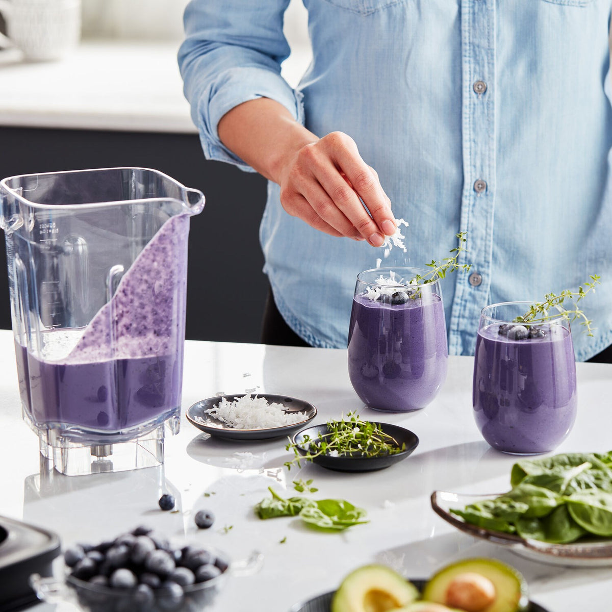Person pouring purple smoothie from blender into cups at the countertop
