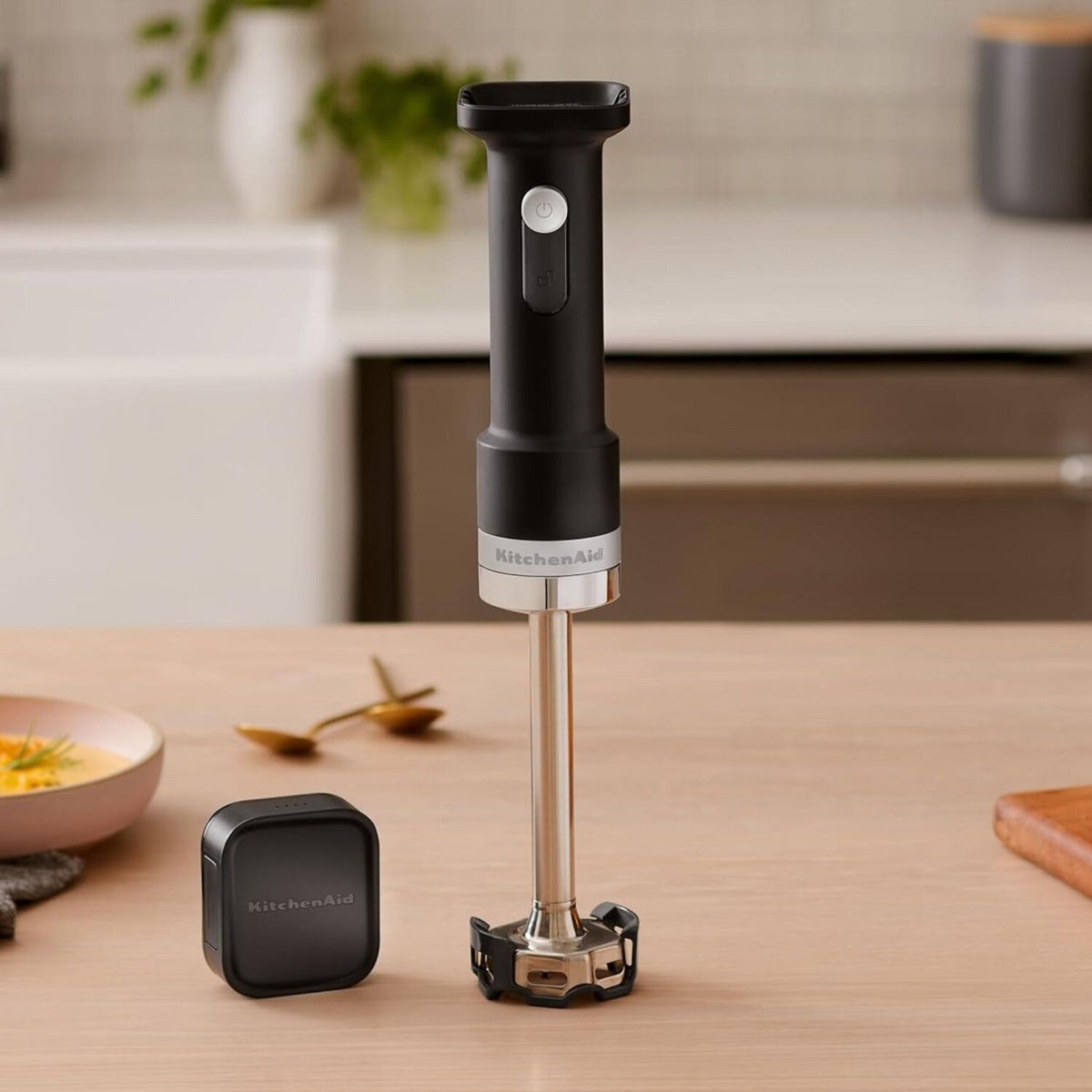 Cordless hand blender with black handle and stainless steel shaft, shown with battery pack.