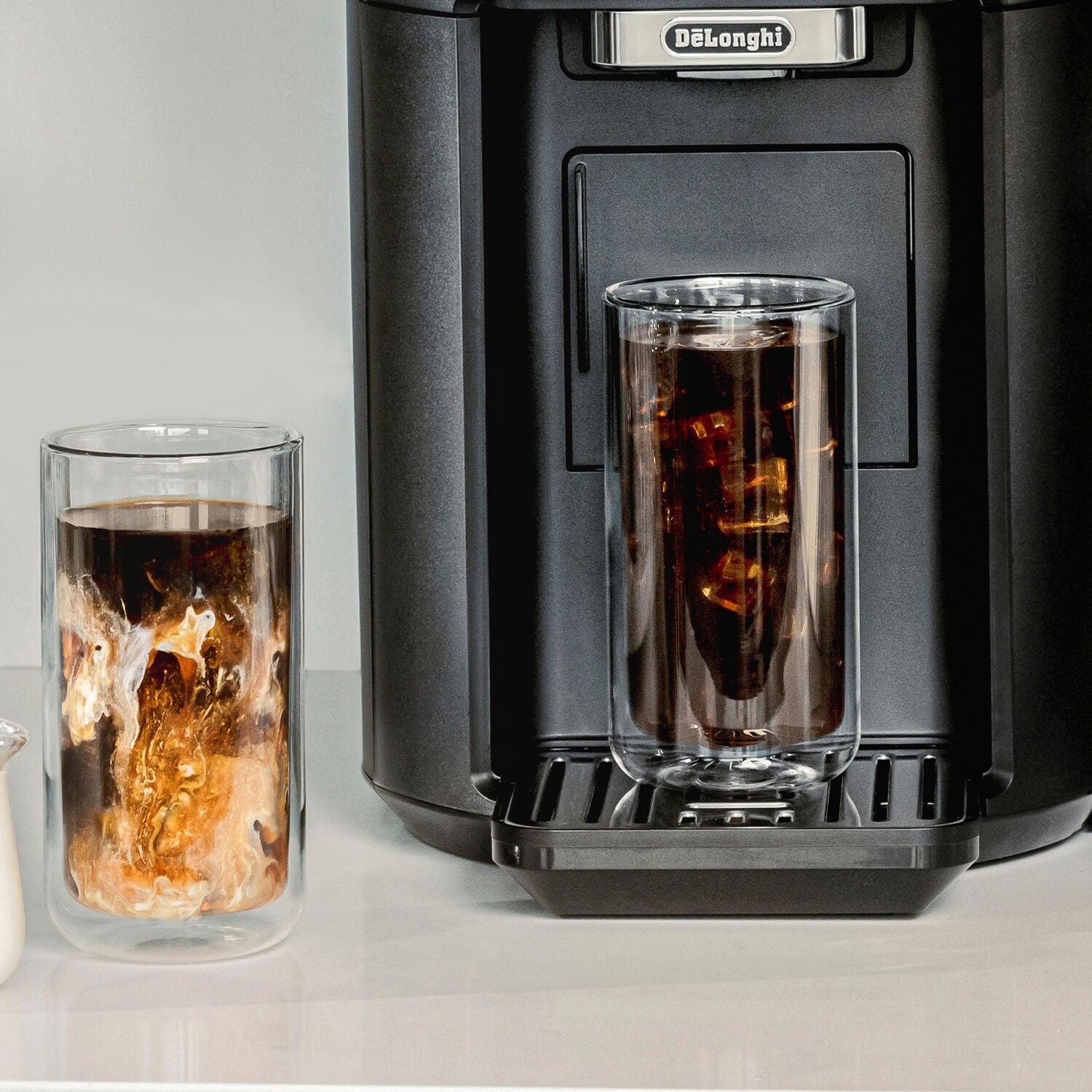 Two double-wall glasses filled with iced coffee, placed near an espresso machine