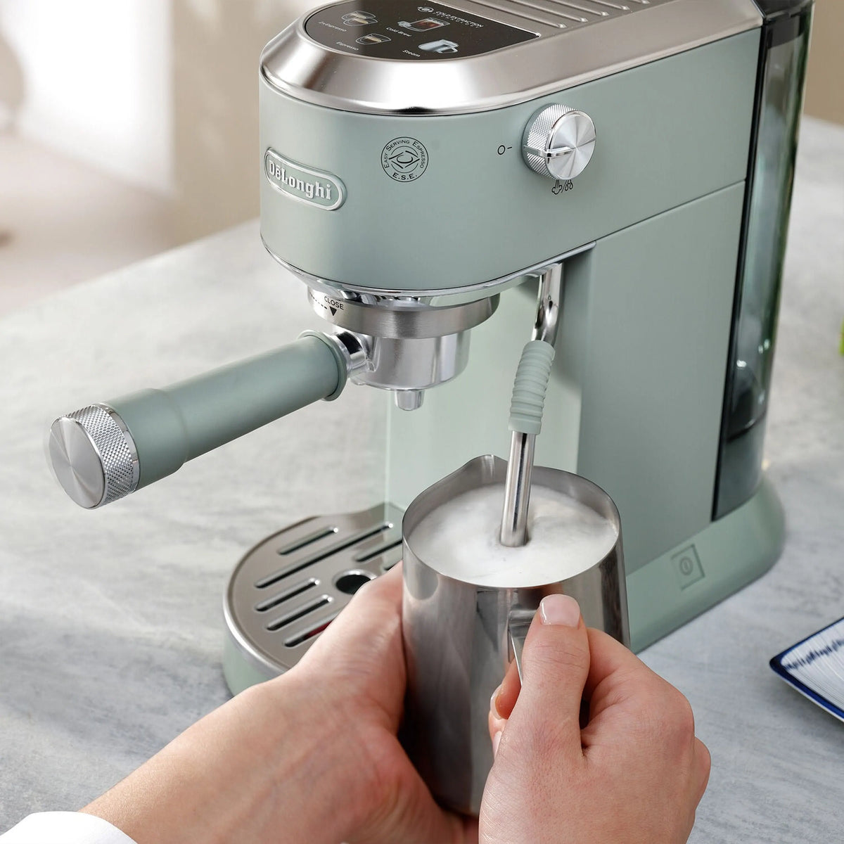 De'Longhi Dedica Duo espresso machine with frothing wand, mint green, hand holding a cup