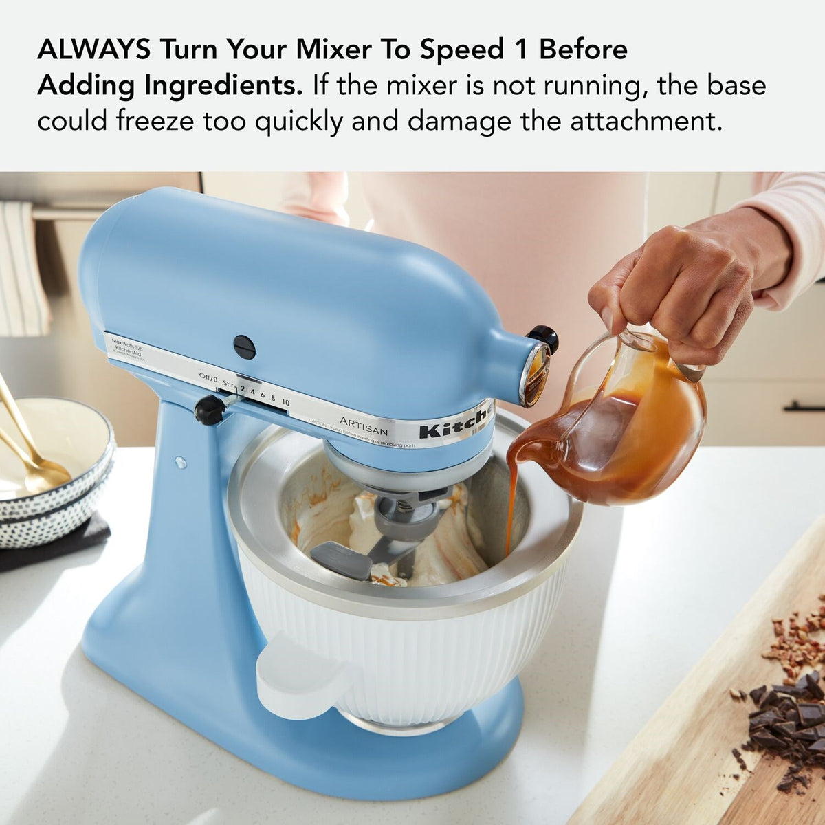 White ice cream maker attachment bowl on blue stand mixer with pour stream