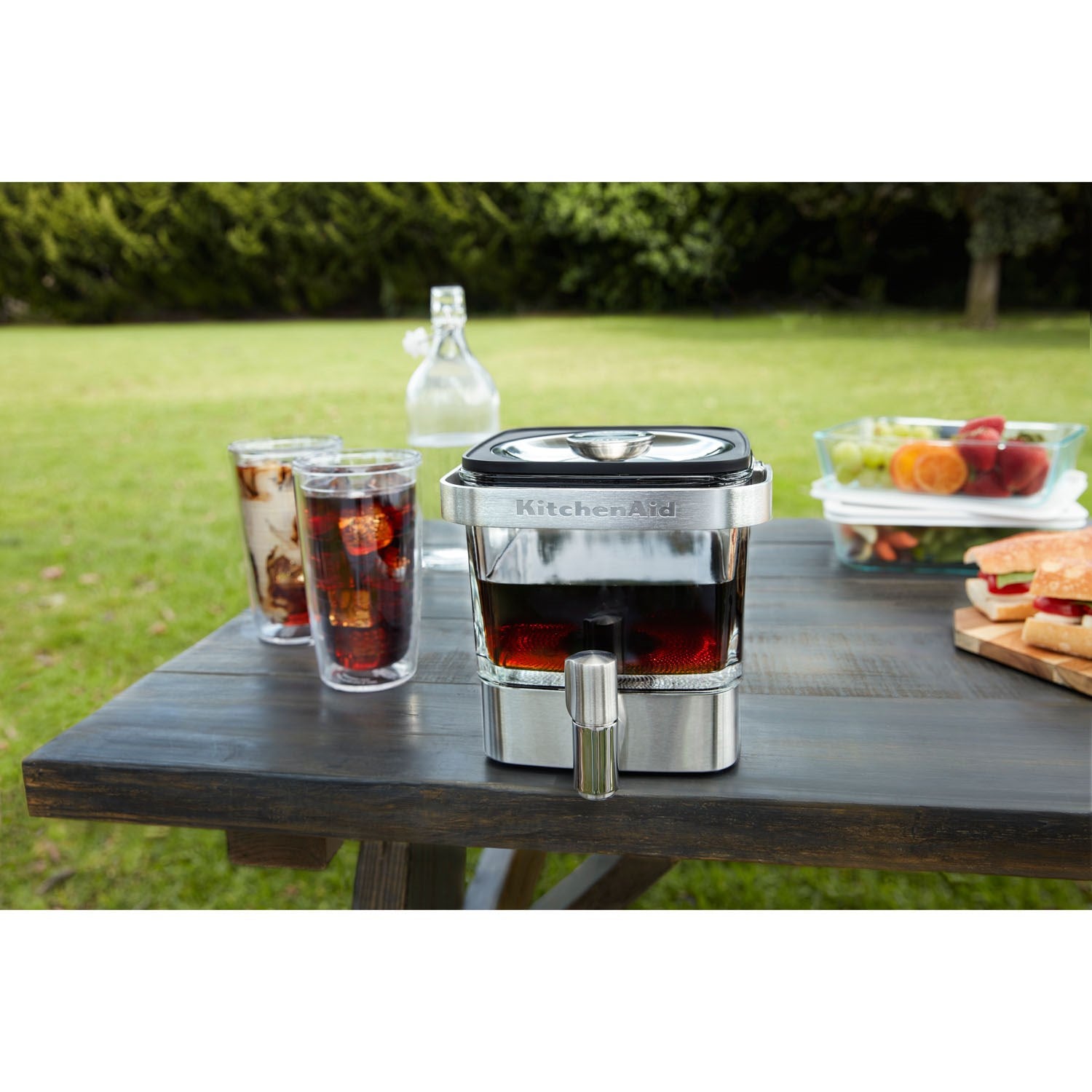 Brushed stainless cold brew maker on outdoor table with coffee glasses