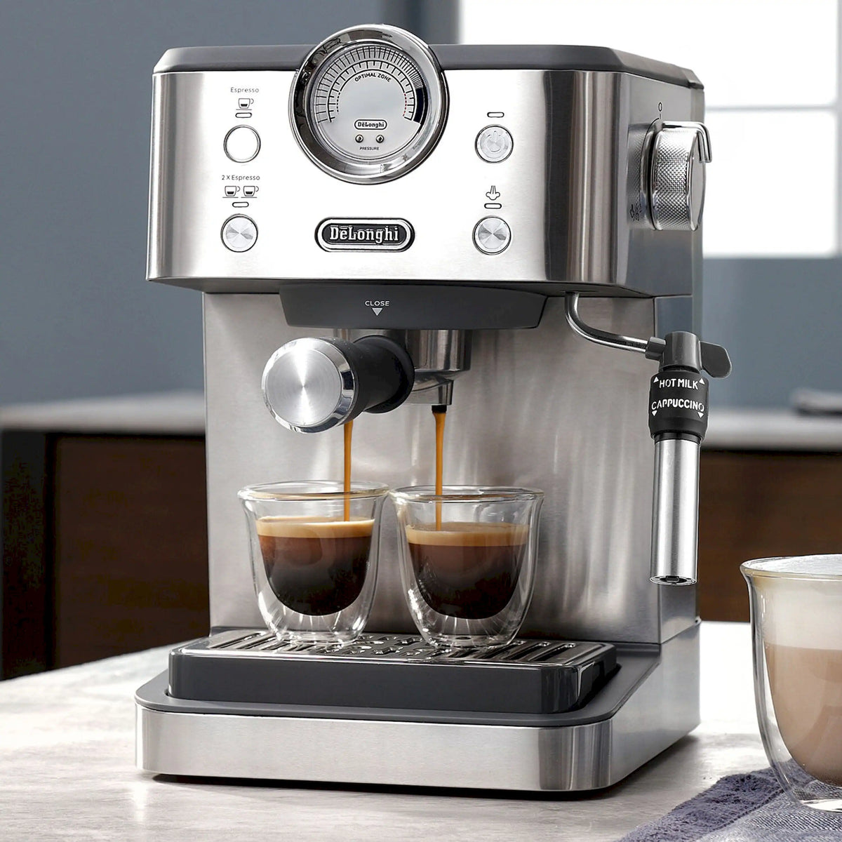 Stainless steel De'Longhi espresso machine brewing from dual spouts into two glass cups
