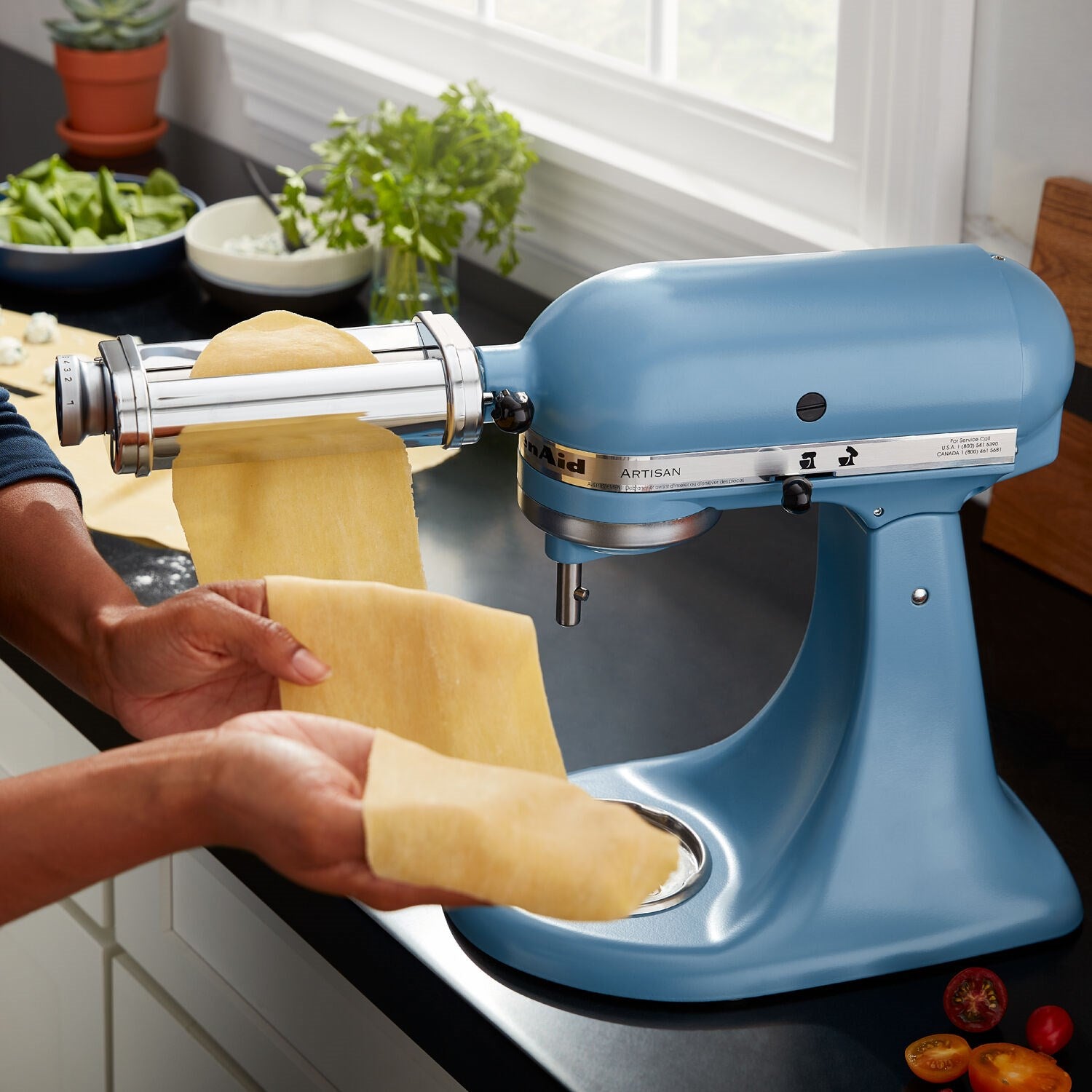 Blue tilt-head stand mixer with pasta attachment rolling dough on the roller