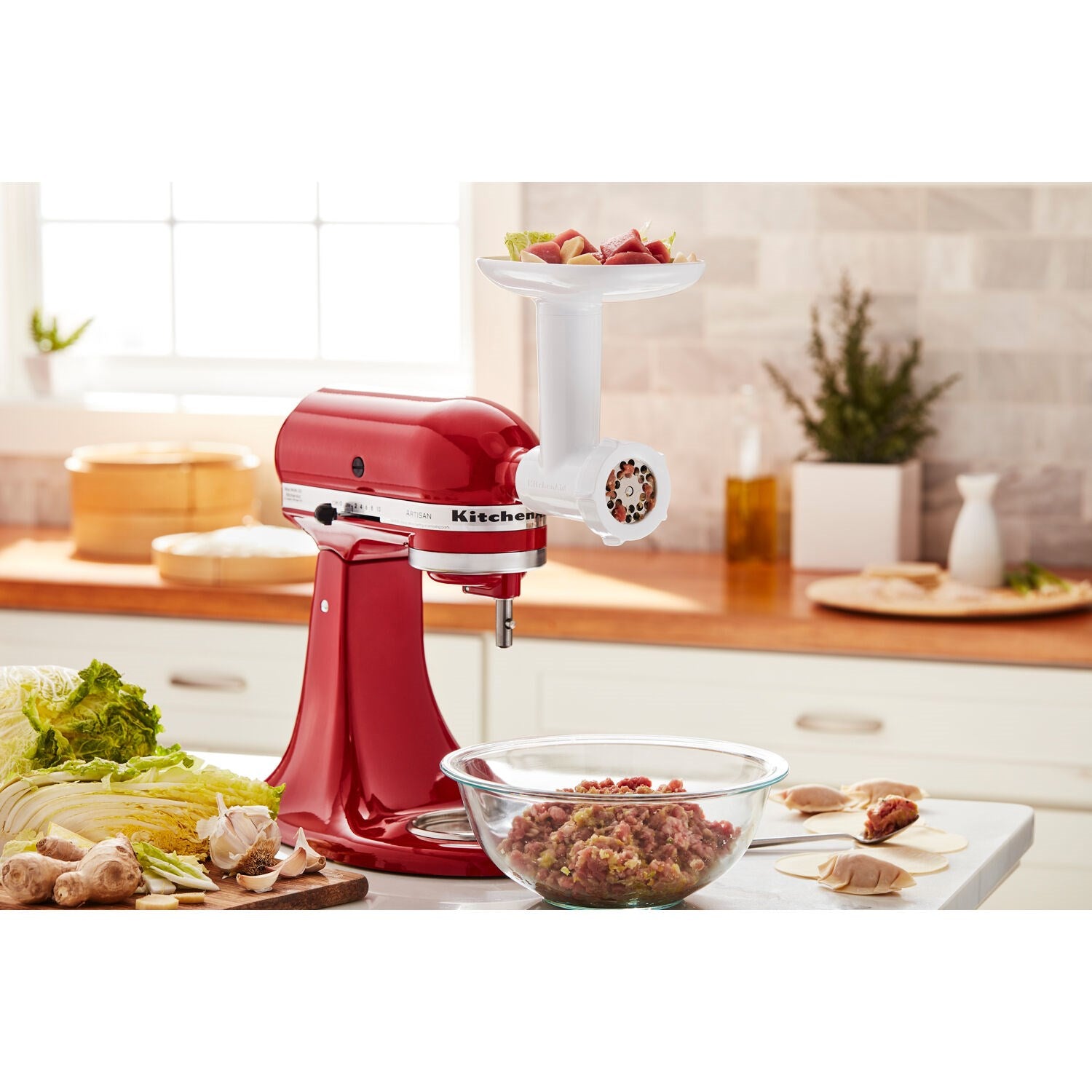 Food grinder attachment on red stand mixer with ingredient tray and grinding plates