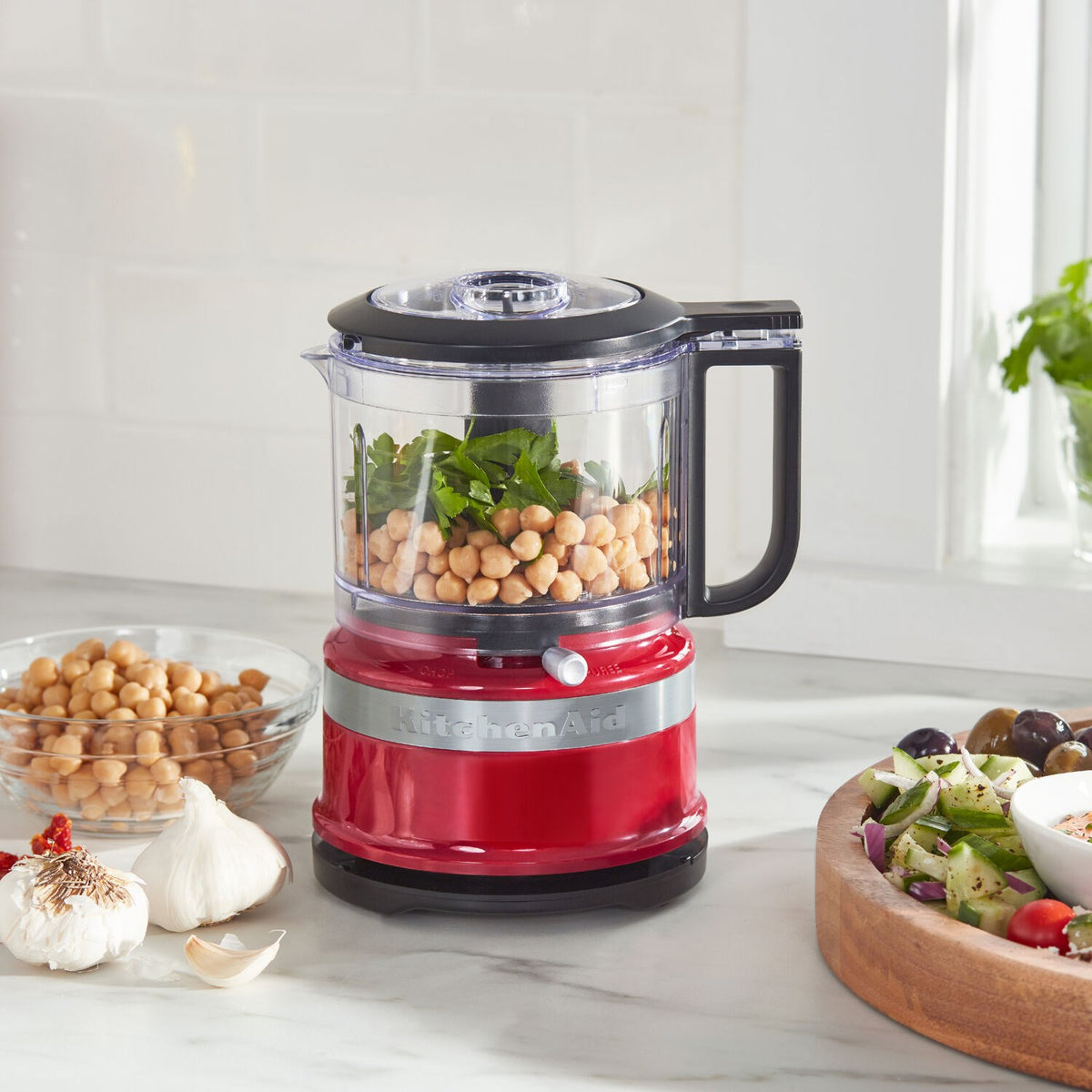 KitchenAid food chopper with clear bowl filled with chickpeas and herbs; Empire Red base