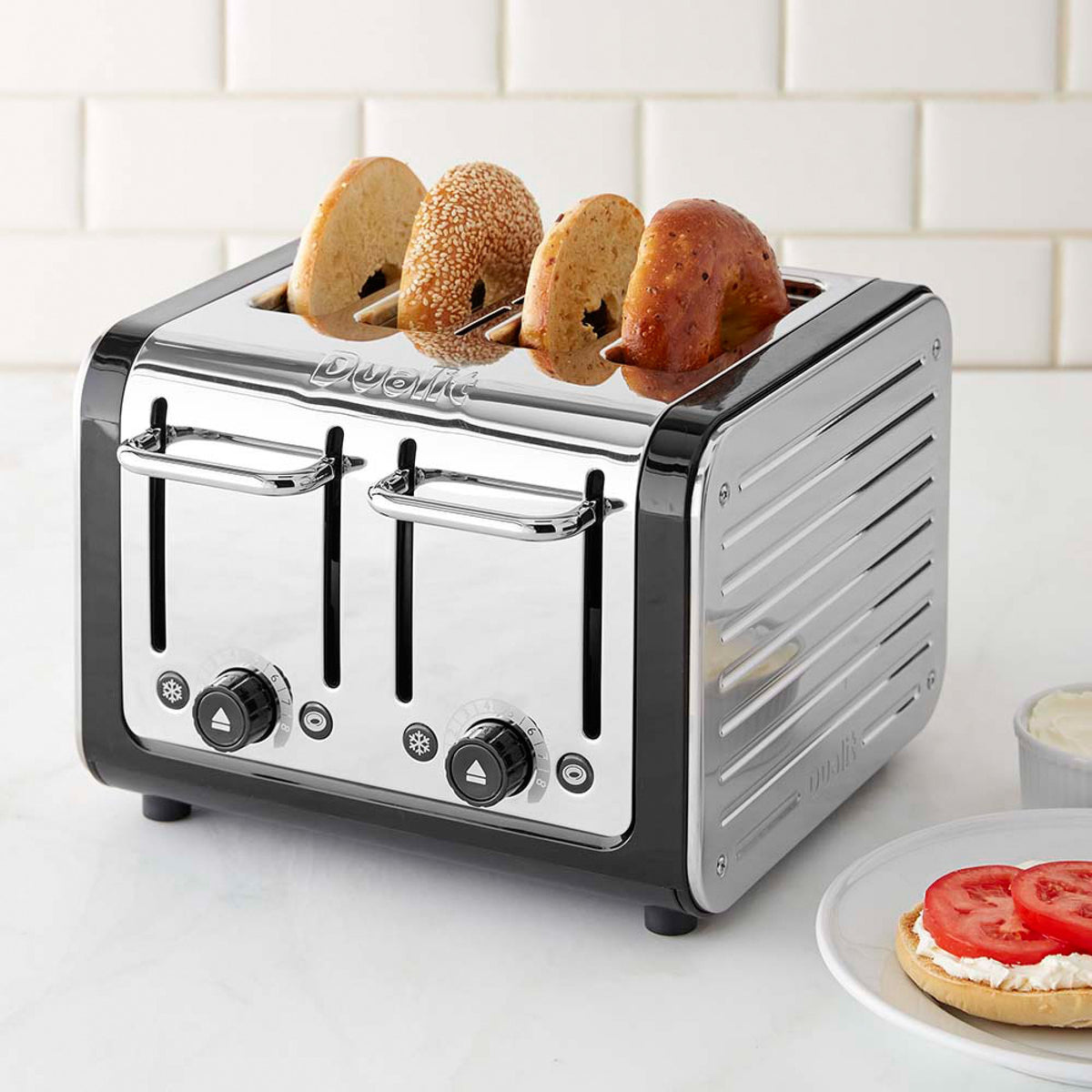 Silver and black 4-slice toaster with bread in the slots on a kitchen counter.
